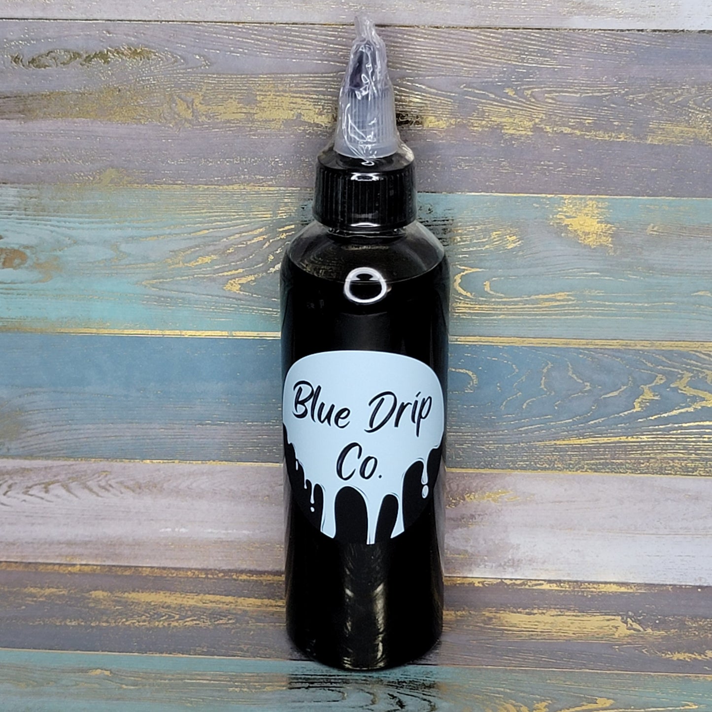 A black bottle with a nozzle top labeled 'Blue Drip Co.' against a textured wooden background.