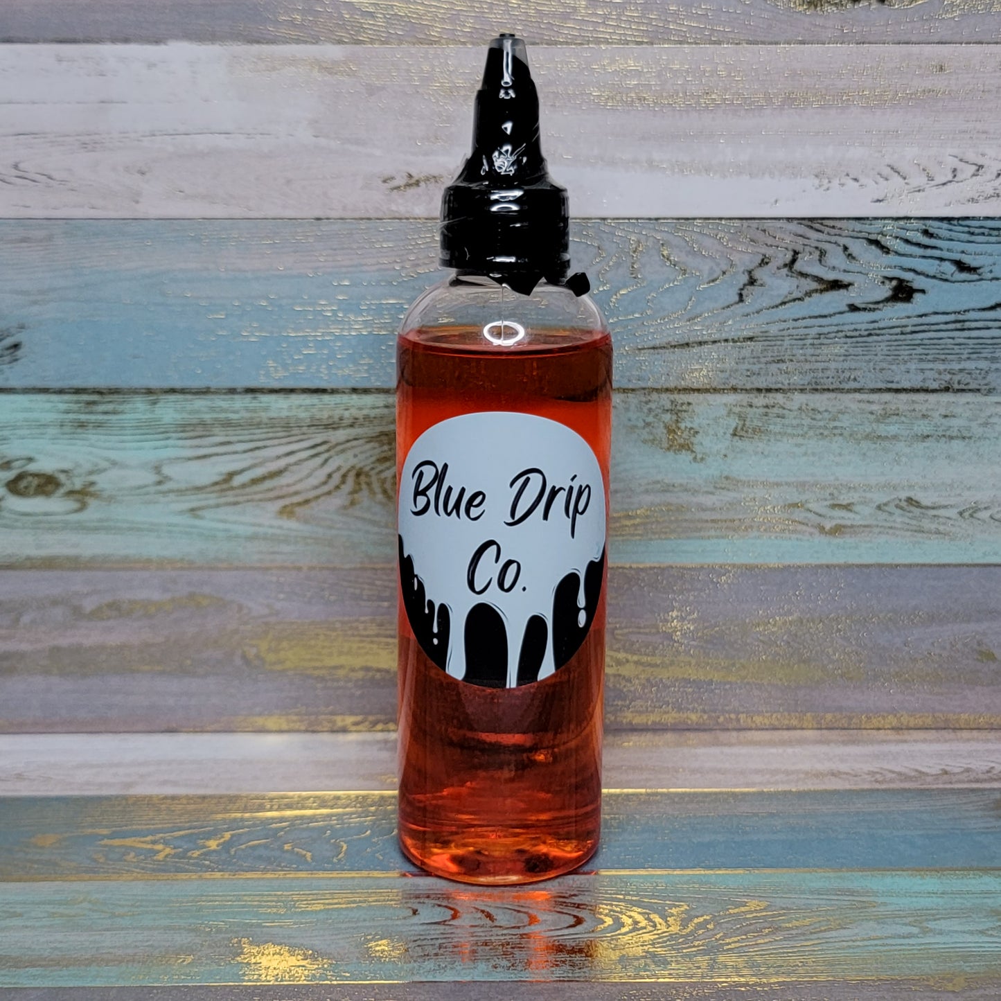 A bottle of liquid labeled 'Blue Drip Co.' with a black and white design on a colorful wooden background.