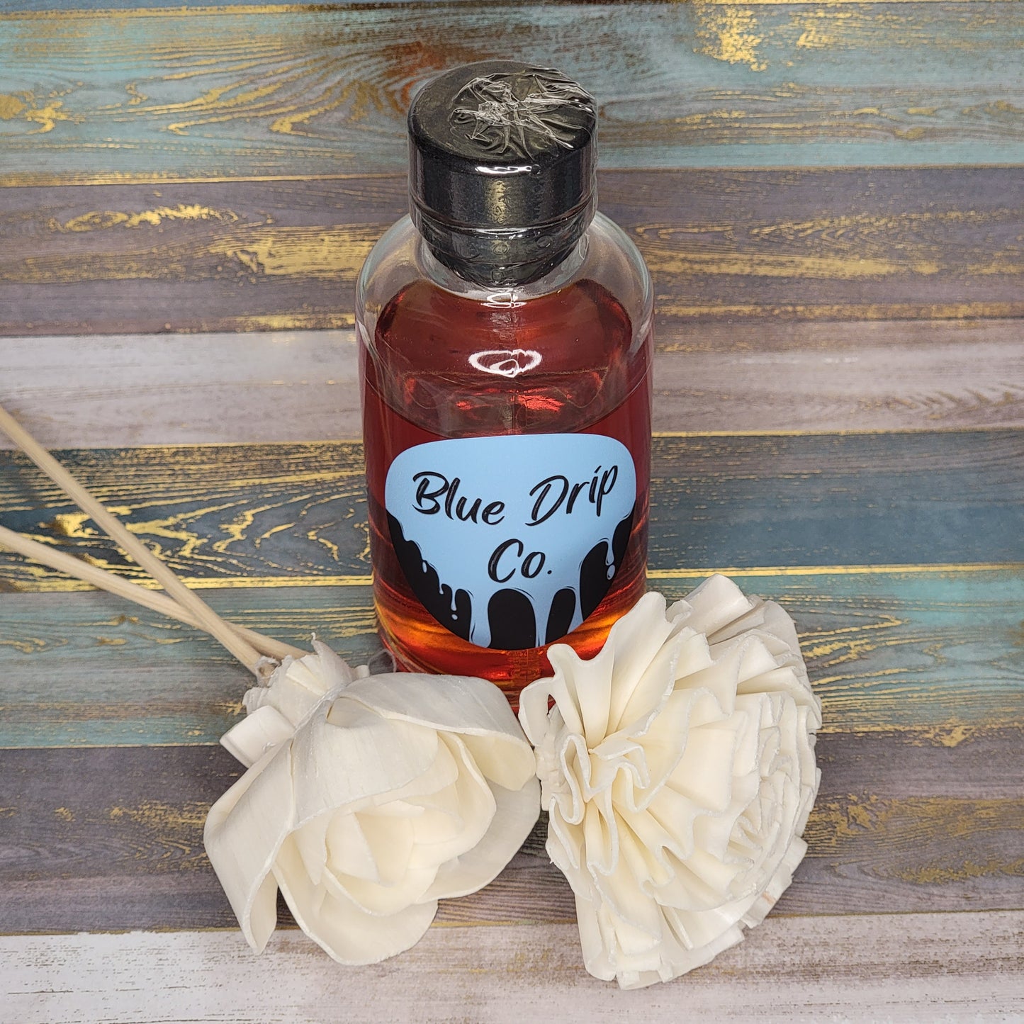 A bottle labeled 'Blue Drip Co.' next to two white fabric flowers on a textured background.