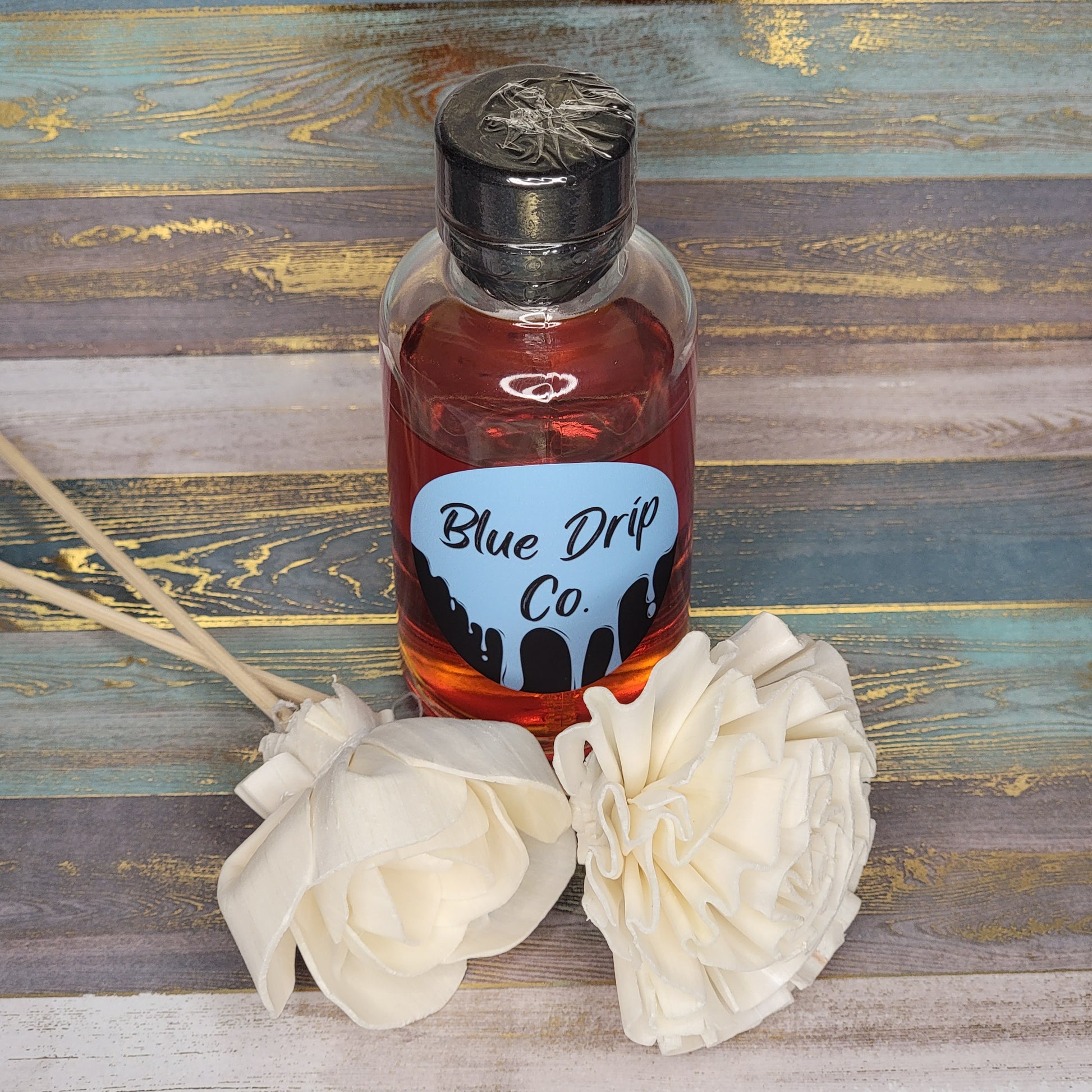 A bottle labeled 'Blue Drip Co.' next to two white fabric flowers on a textured background.