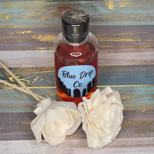 A bottle labeled 'Blue Drip Co.' next to two white fabric flowers on a textured background.