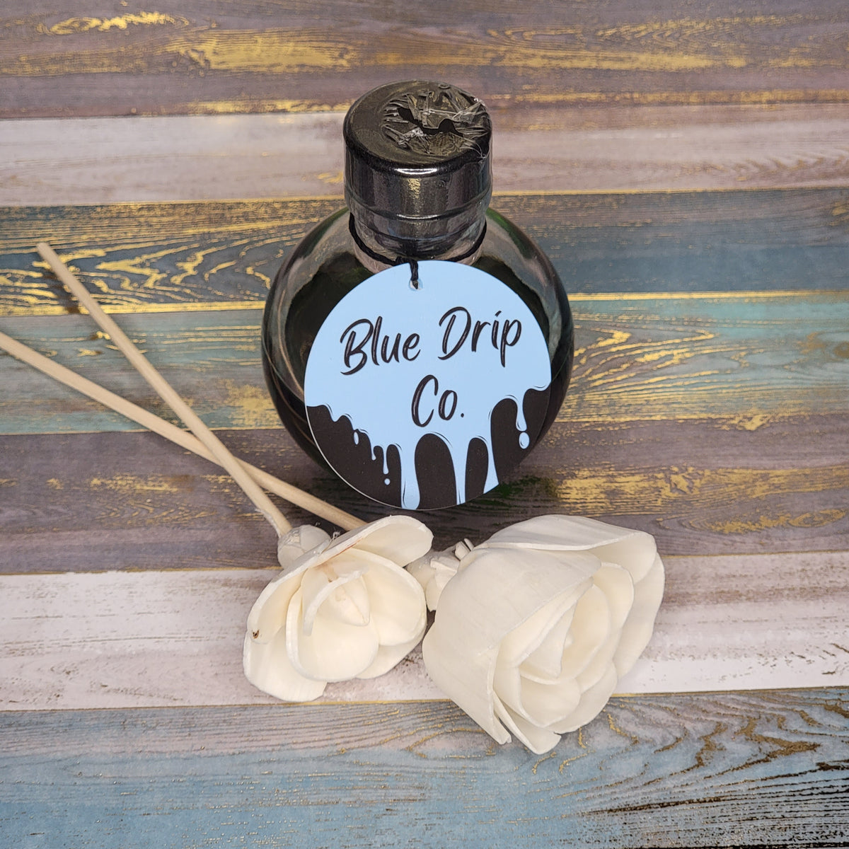 Bottle labeled 'Blue Drip Co.' beside white roses on a wooden surface.