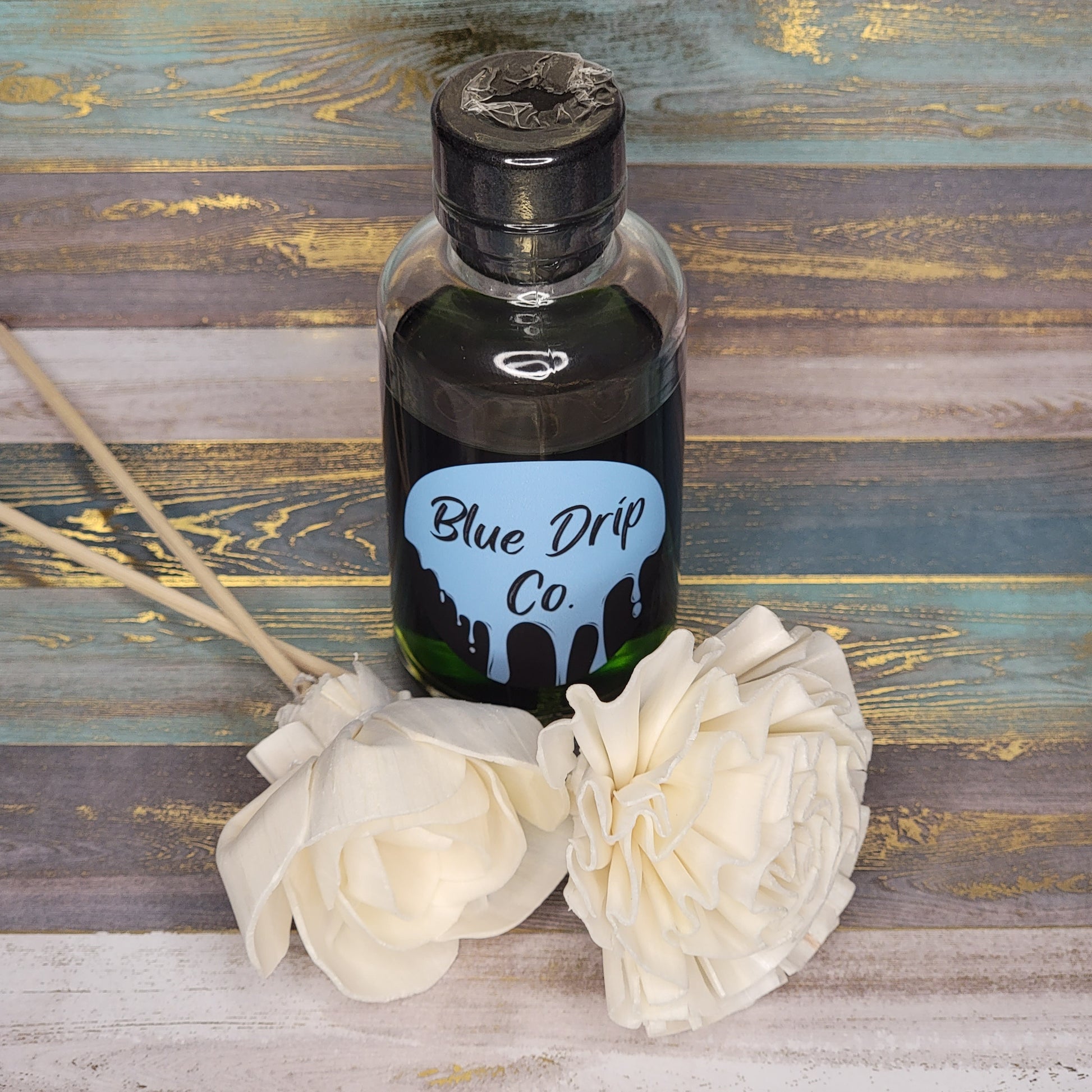 A bottle of scented oil from Blue Drip Co. with decorative white flowers beside it.