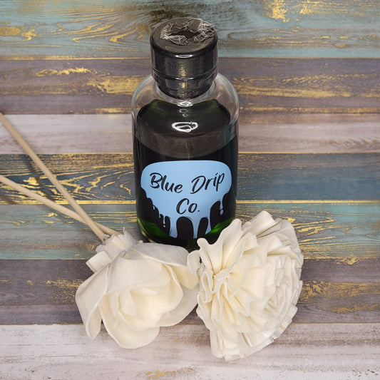 A bottle of scented oil from Blue Drip Co. with decorative white flowers beside it.