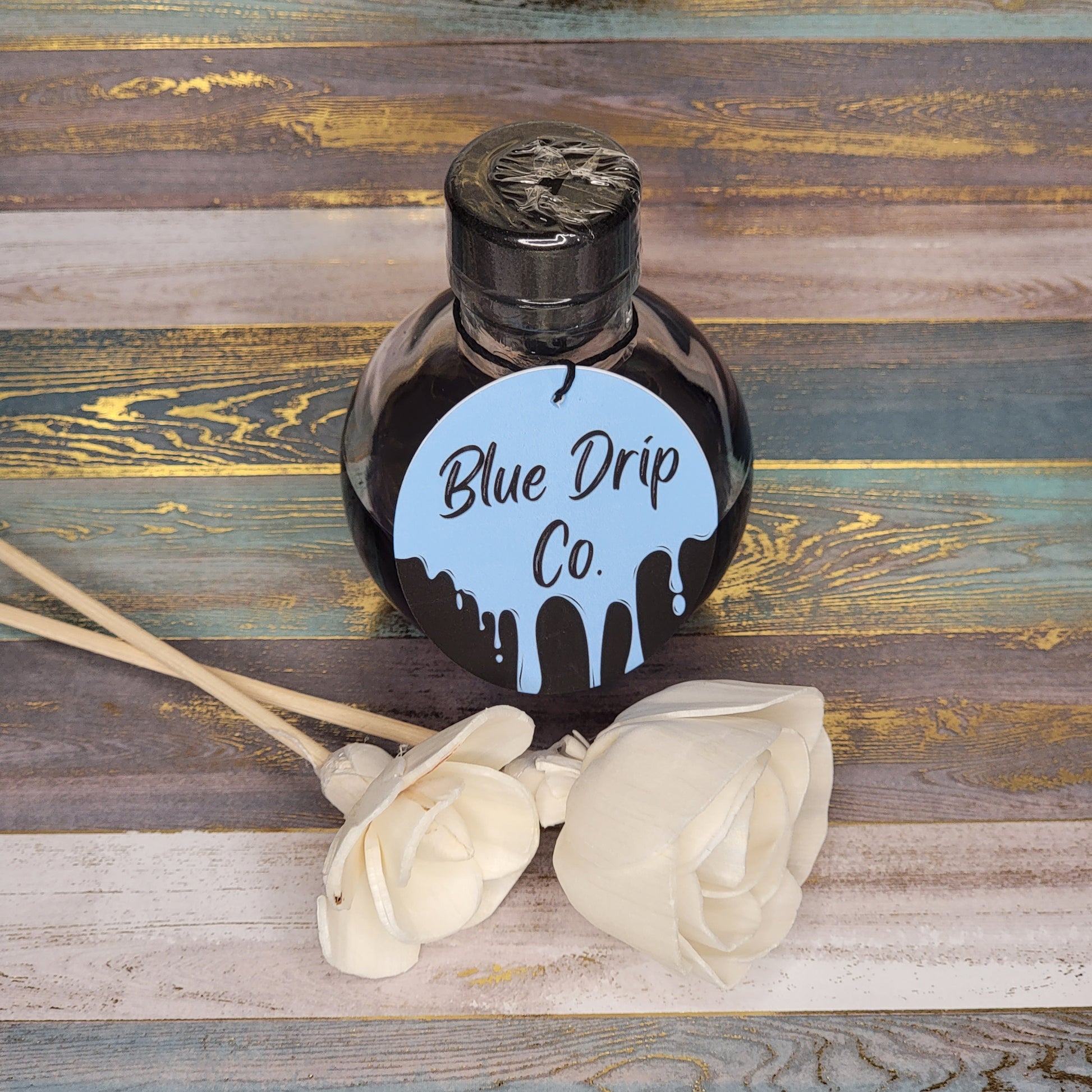 Bottle labeled 'Blue Drip Co.' with decorative white roses on a wooden surface.
