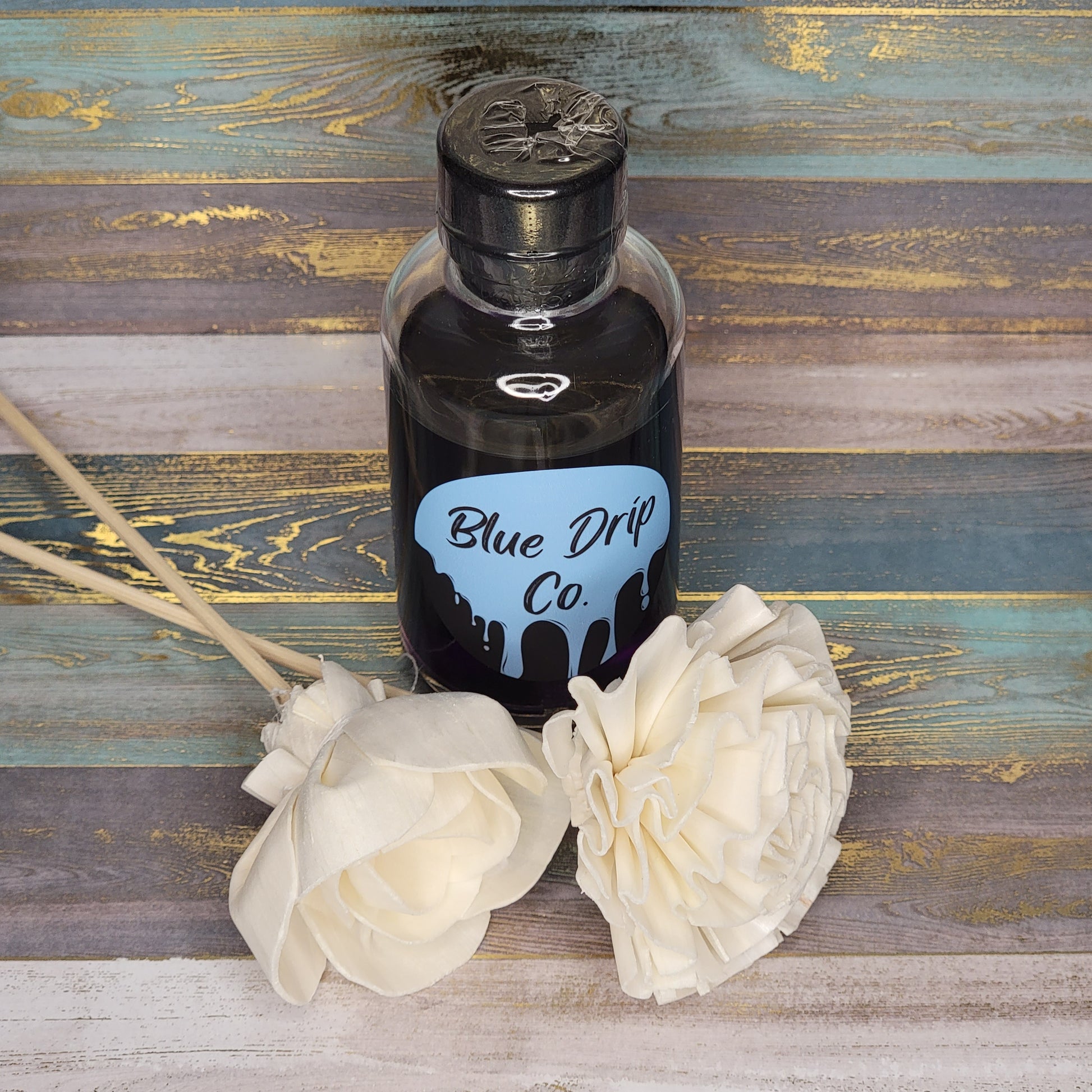 A bottle labeled 'Blue Drip Co.' surrounded by cream-colored decorative flowers.