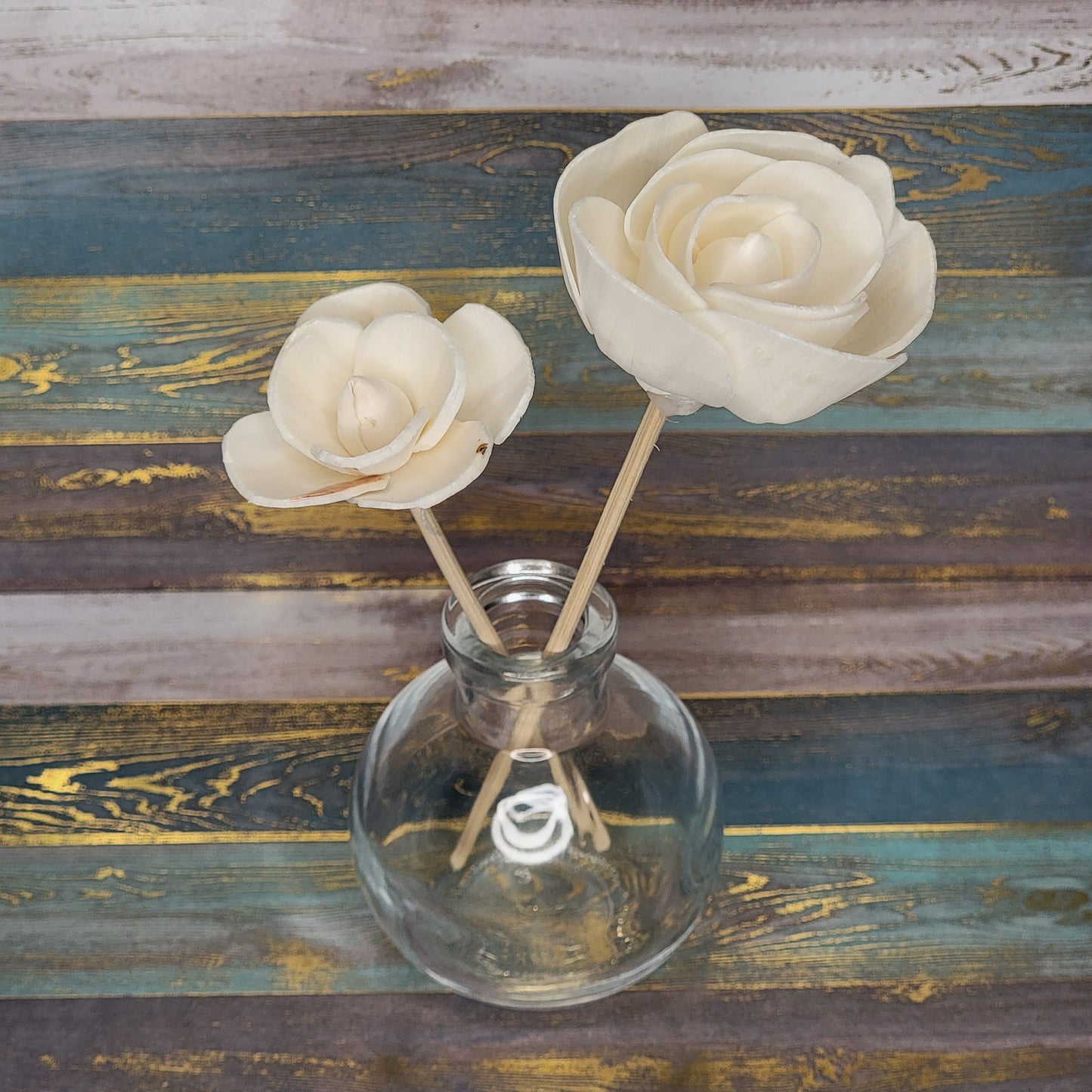Two decorative cream-colored flowers in a glass vase on a wooden surface.