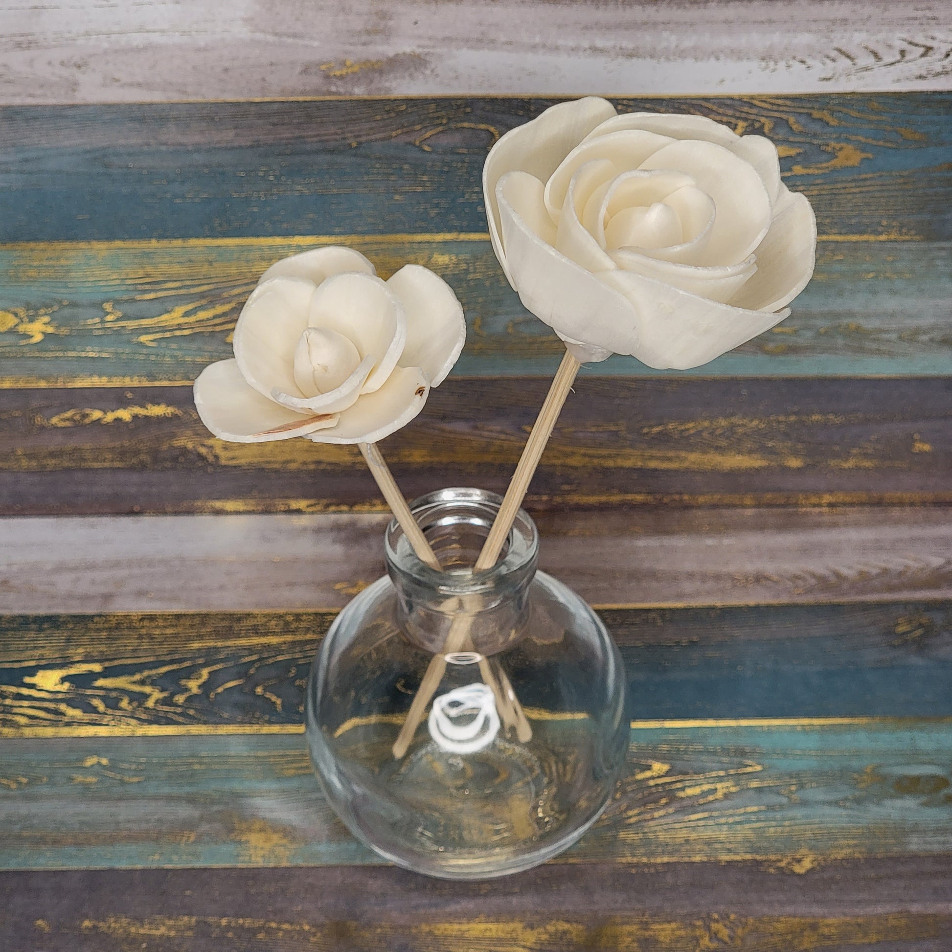 Two decorative cream-colored flowers in a glass vase on a wooden surface.