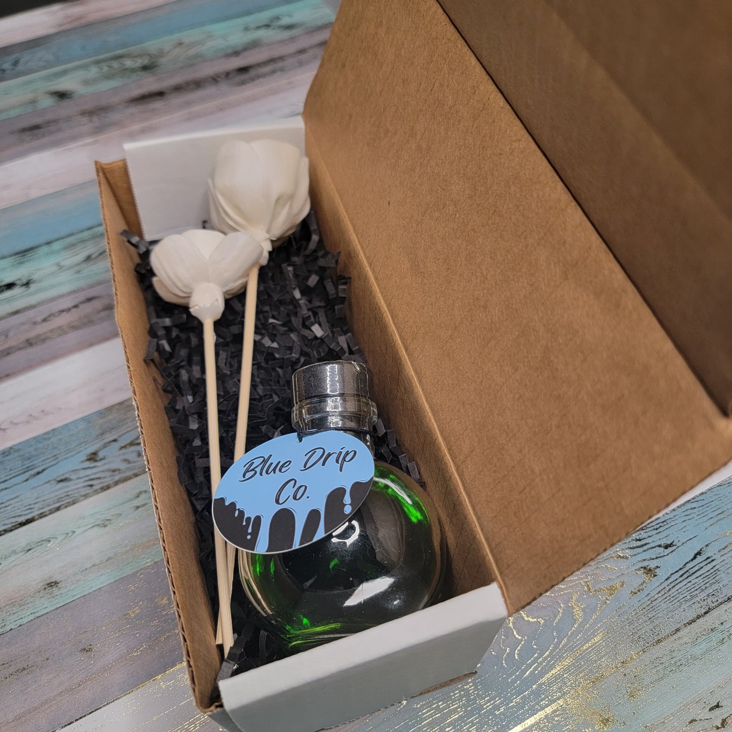 A closed box containing a green liquid bottle, a tag marked 'Blue Drip Co', and decorative lollipops.