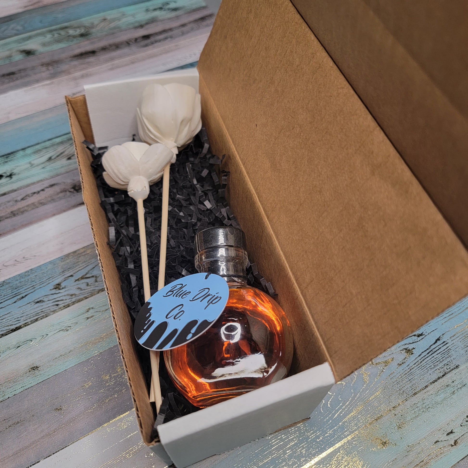 A gift box containing a bottle of perfume and two decorative objects on a bed of crinkle paper.