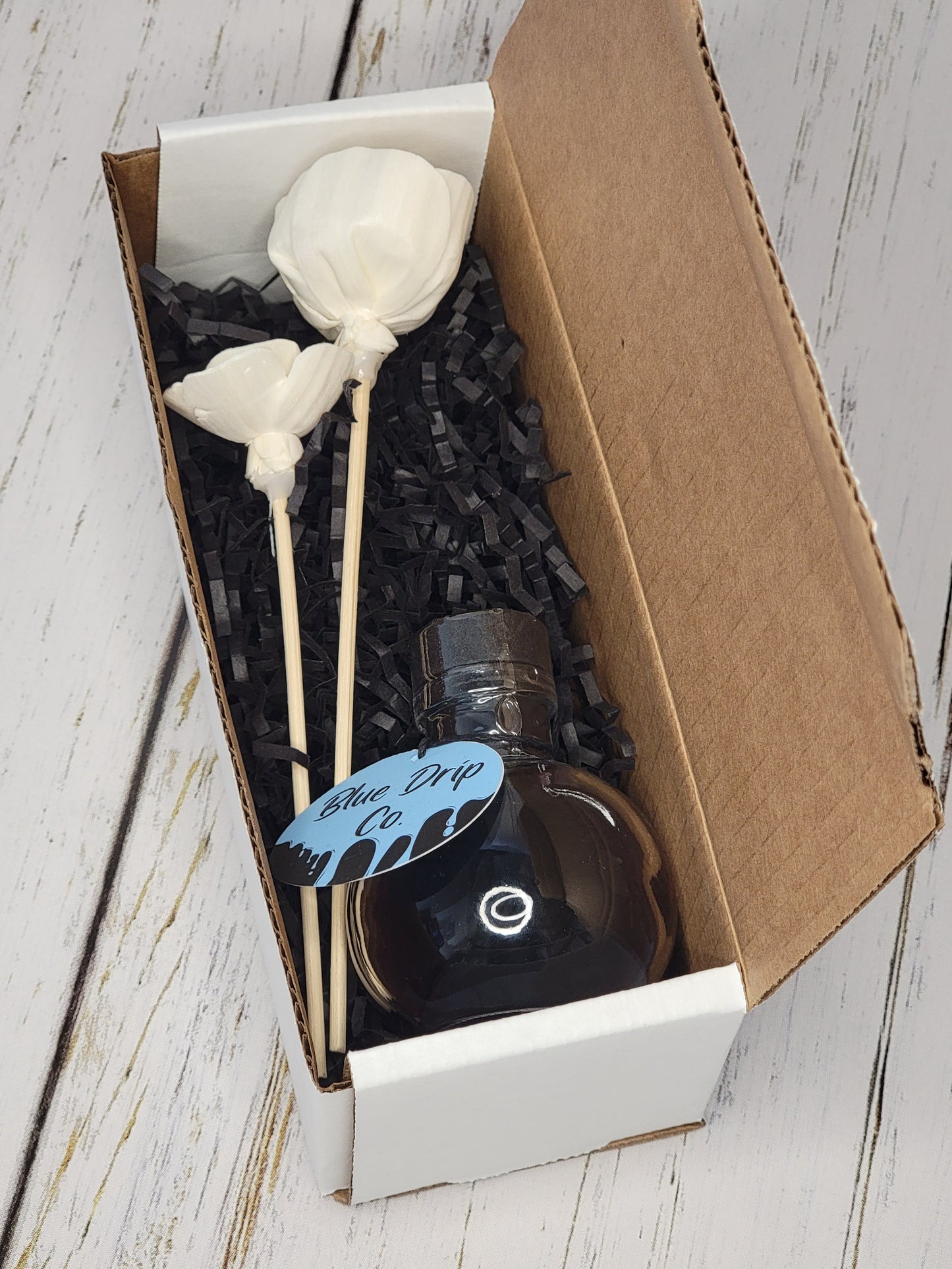 A box containing a bottle and two decorative sticks with white flowers.