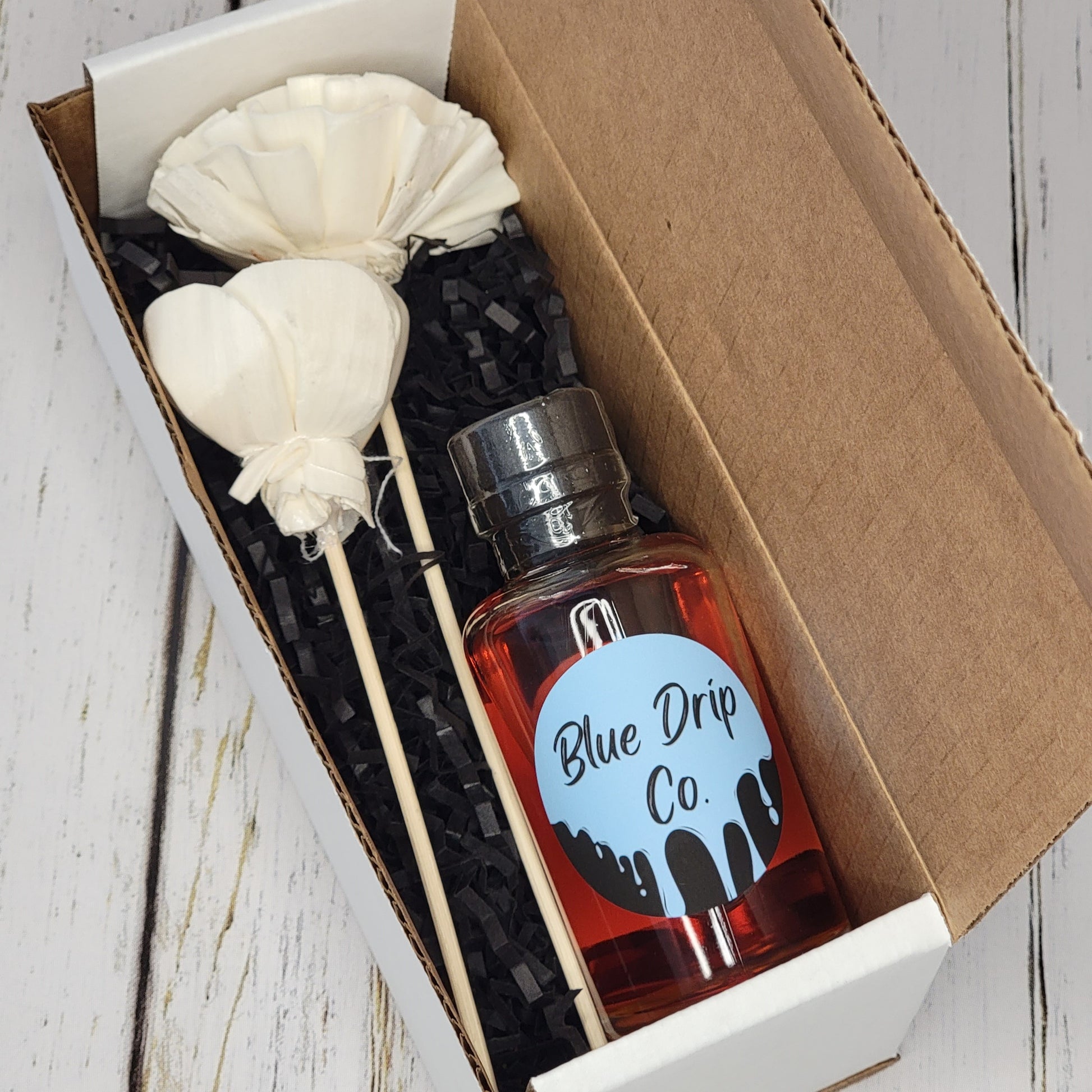A gift box containing a bottle labeled 'Blue Drip Co.' and decorative items.