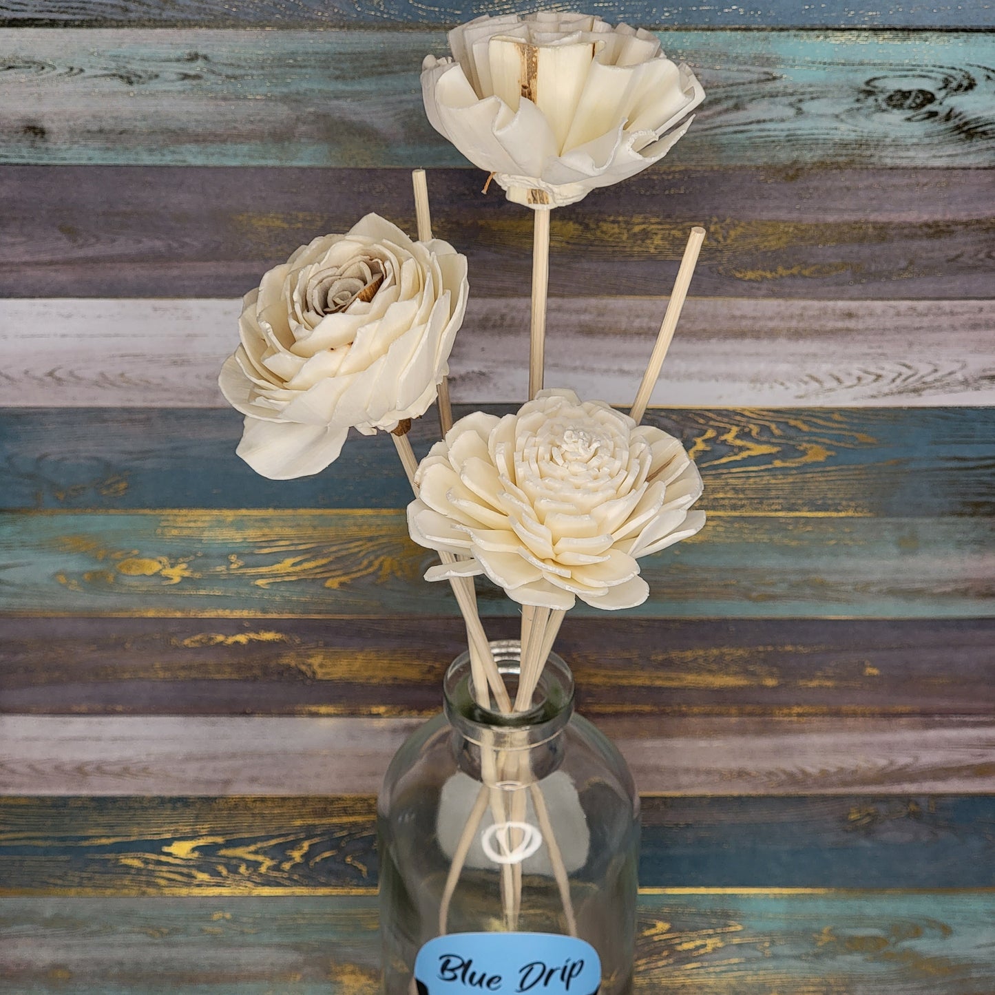 A decorative arrangement of cream-colored flowers in a glass vase against a colorful wooden background.