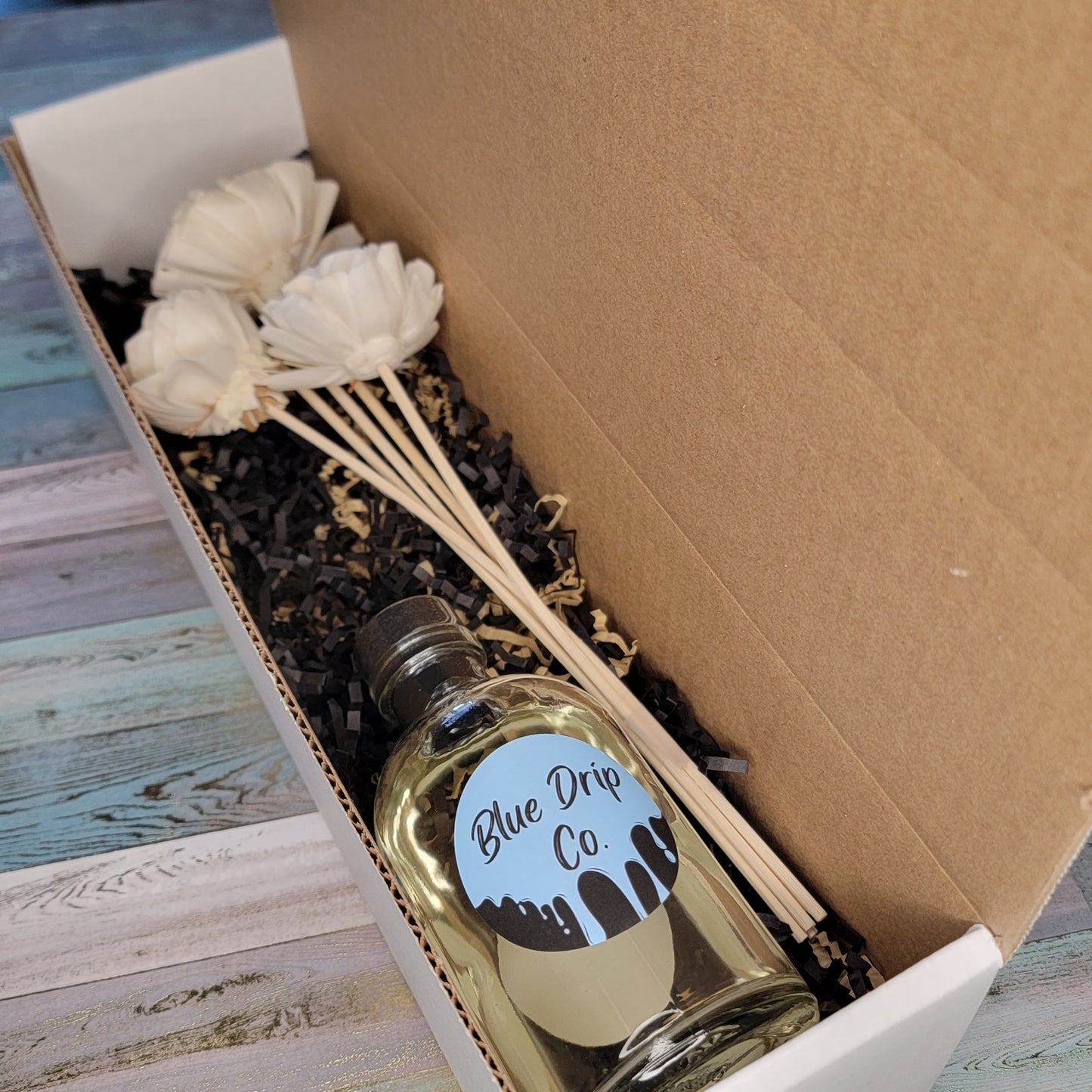 A boxed gift set containing a bottle labeled 'Blue Drip Co.' and decorative flowers.