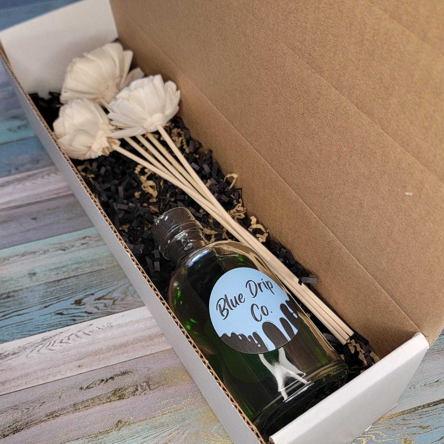 A boxed gift set featuring a bottle labeled 'Blue Drip Co' and decorative white dried flowers.