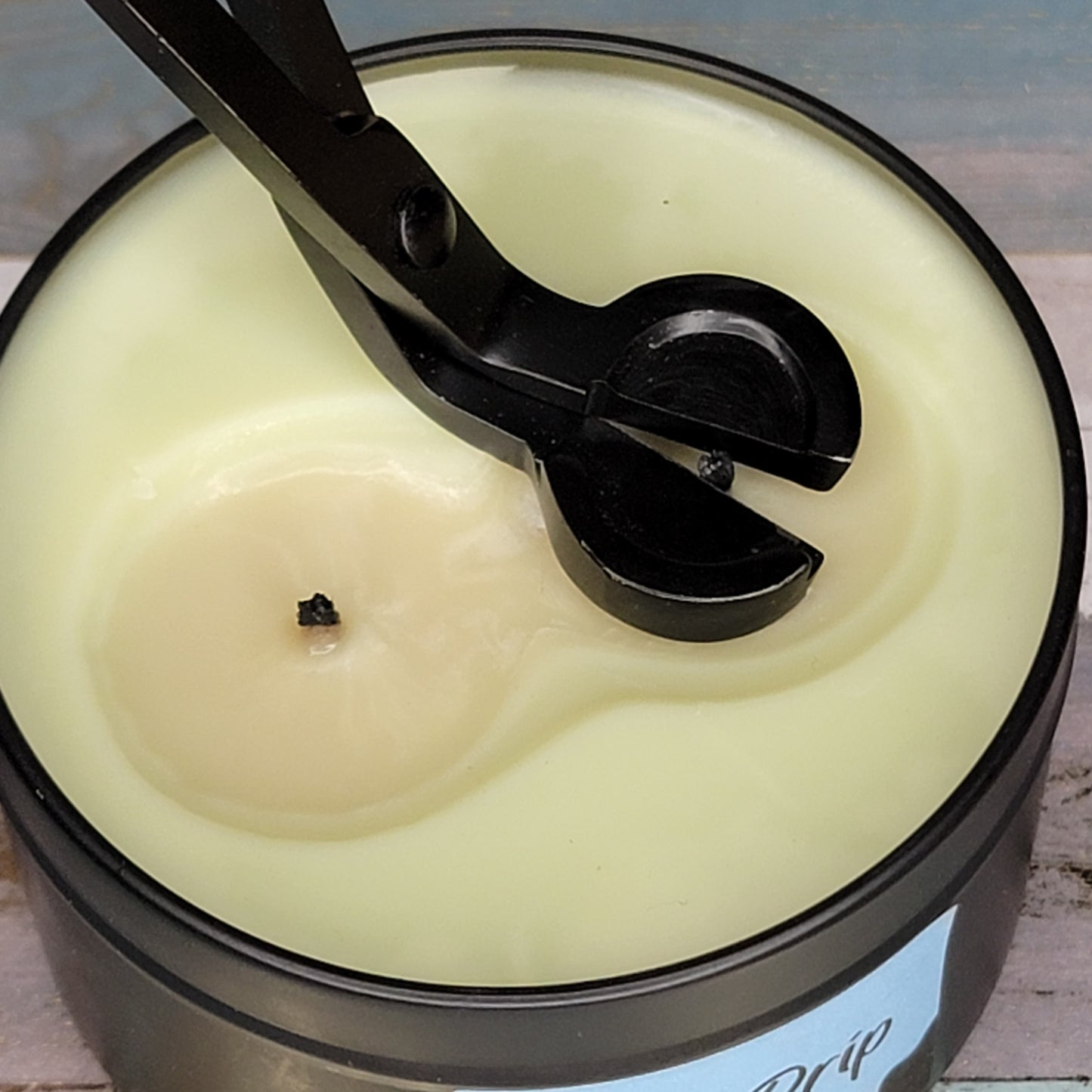 Candle wick trimmer resting on the surface of a cream-colored candle