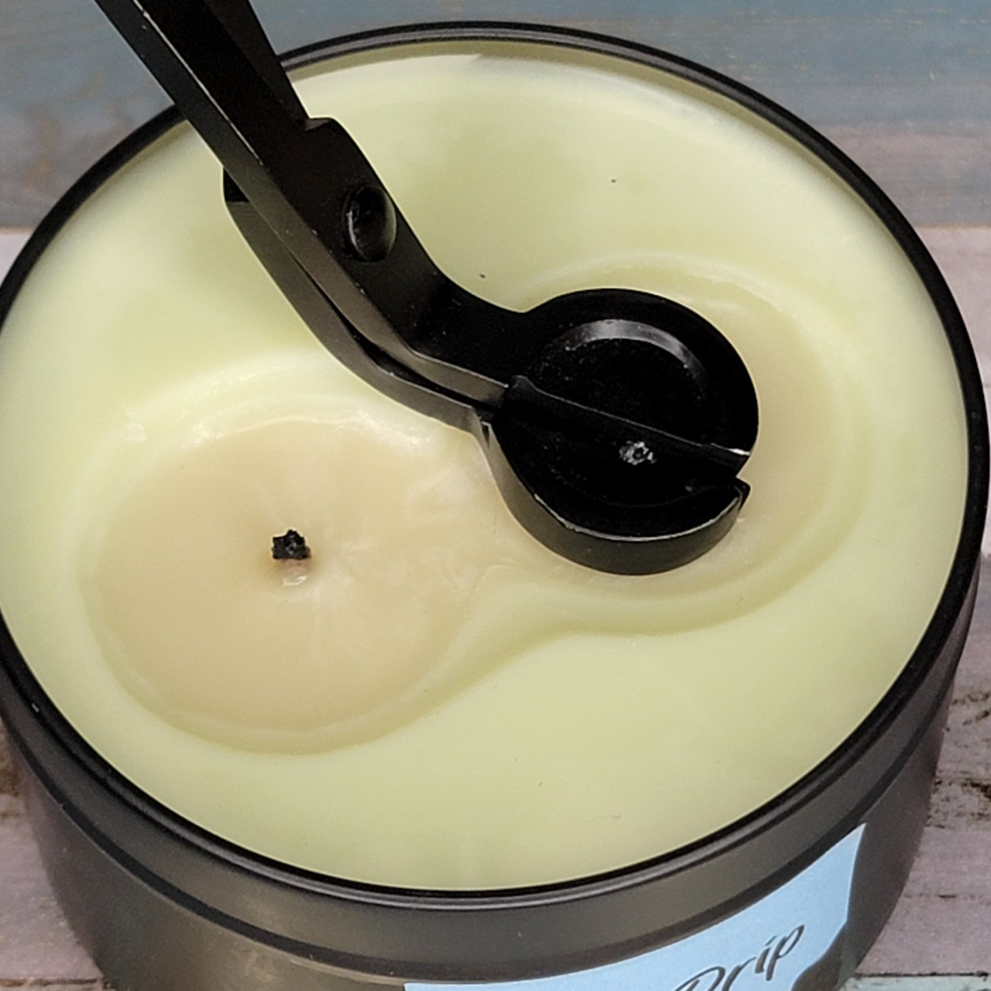 Close-up of a candle with a black wick cutter resting on top of a creamy yellow surface.