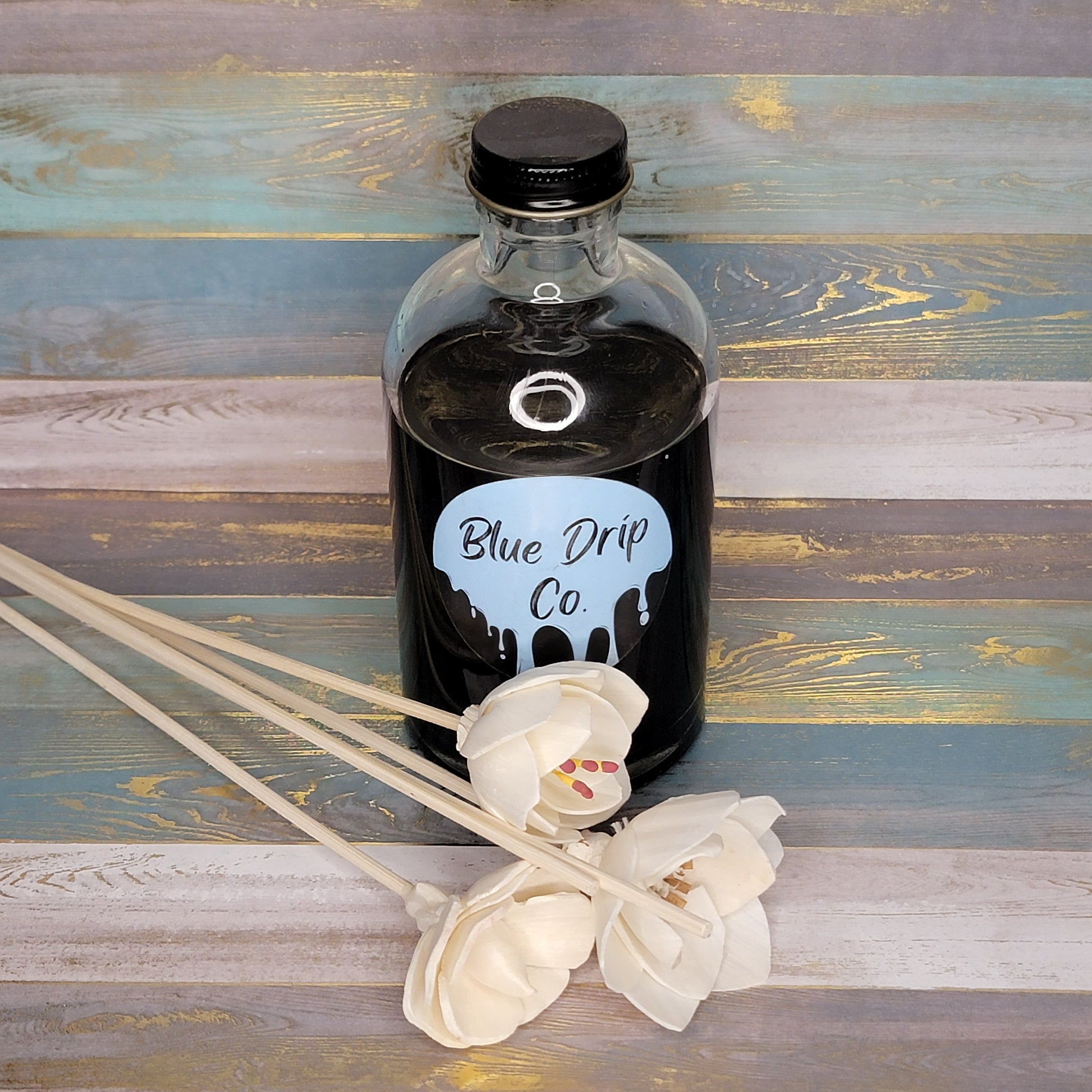 A bottle labeled 'Blue Drip Co.' next to white decorative flowers on a rustic wooden surface.
