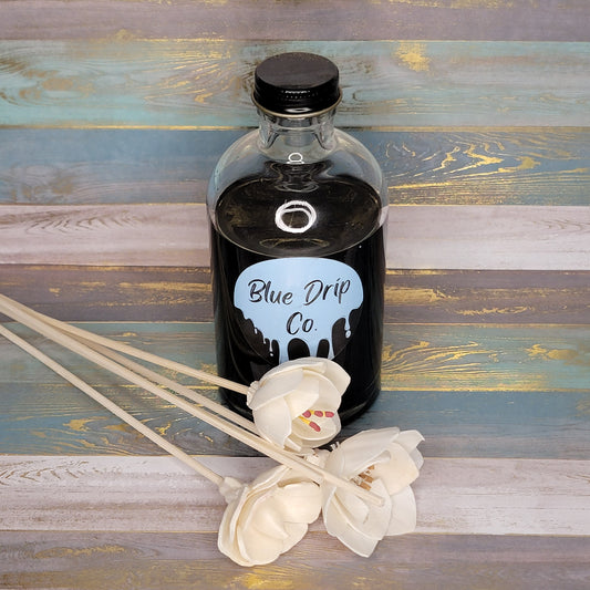 A bottle labeled 'Blue Drip Co.' next to white decorative flowers on a rustic wooden surface.