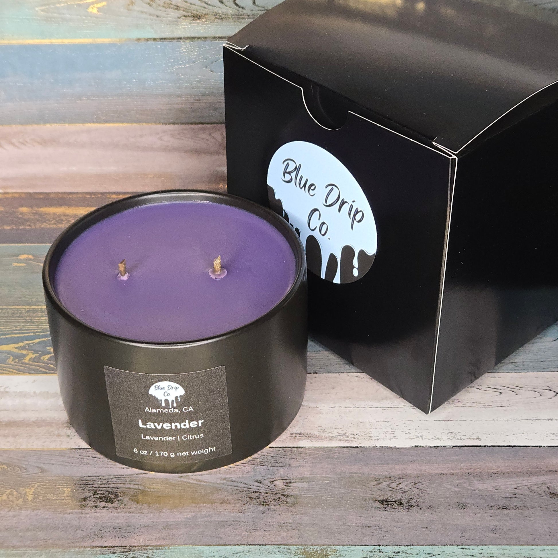 A black candle labeled 'Lavender' beside its packaging from Blue Drip Co