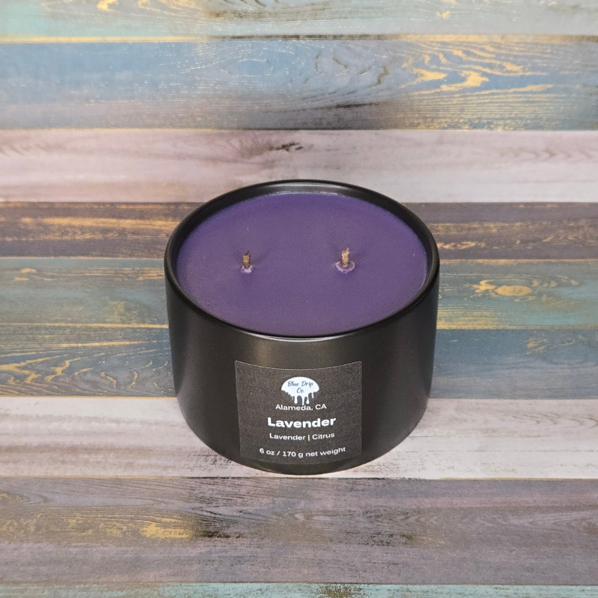A round black candle container with lavender wax and two wicks on a colorful wooden background.