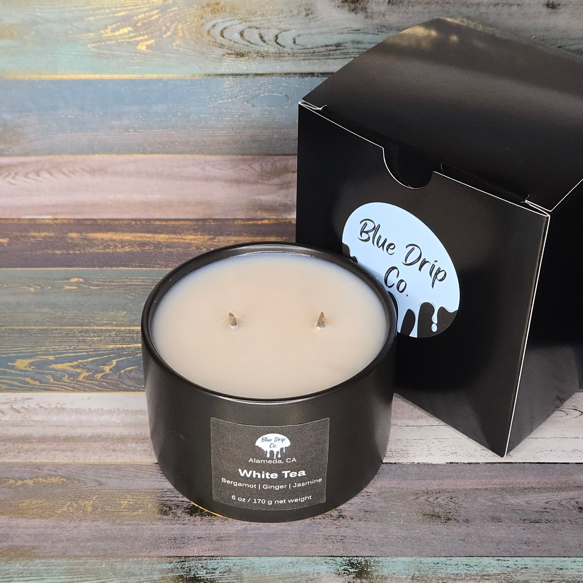 A black candle labeled 'White Tea' next to its packaging from Blue Drip Co.