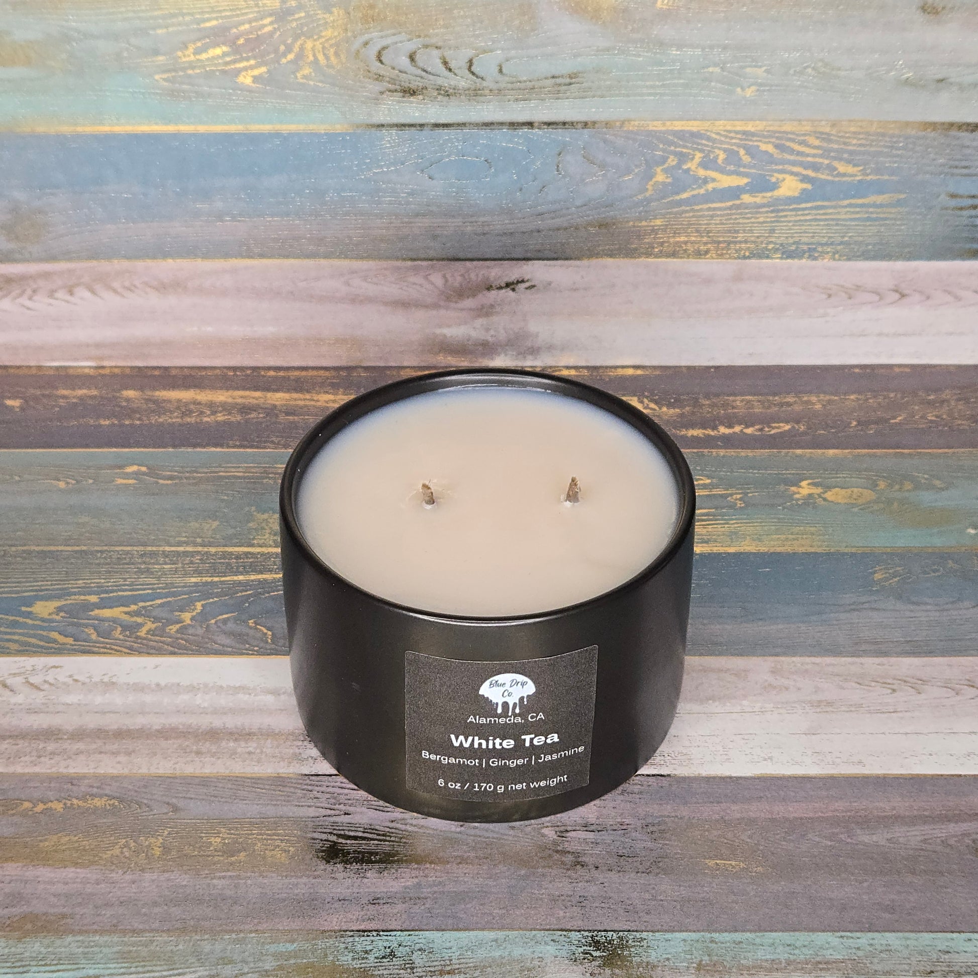 Black candle labeled 'White Tea' on a colorful wooden background