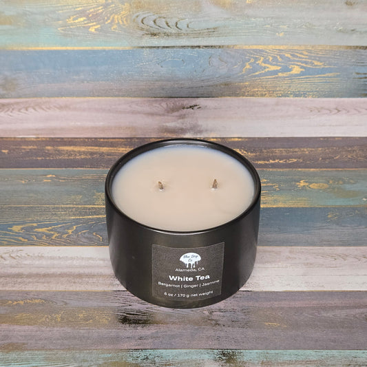 Black candle labeled 'White Tea' on a colorful wooden background