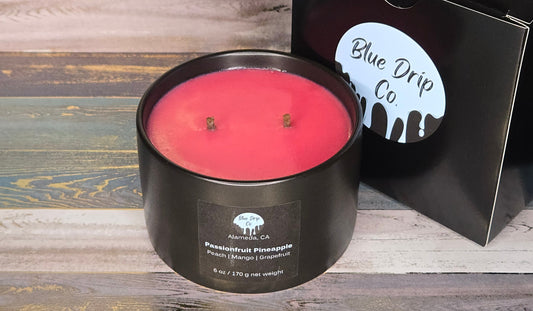 A pink scented candle in a black container next to its packaging from Blue Drip Co.