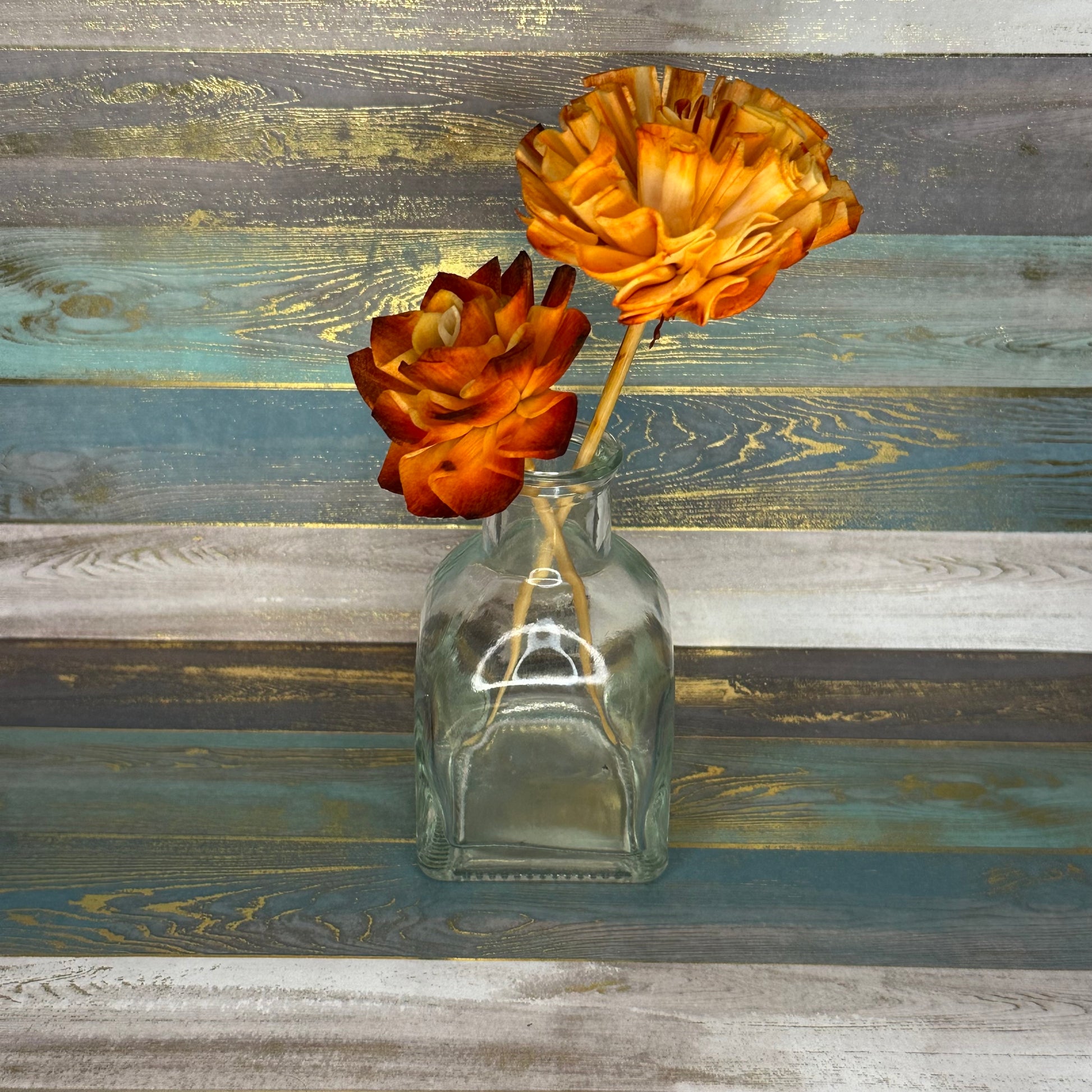 A glass vase with two orange flowers against a textured background.