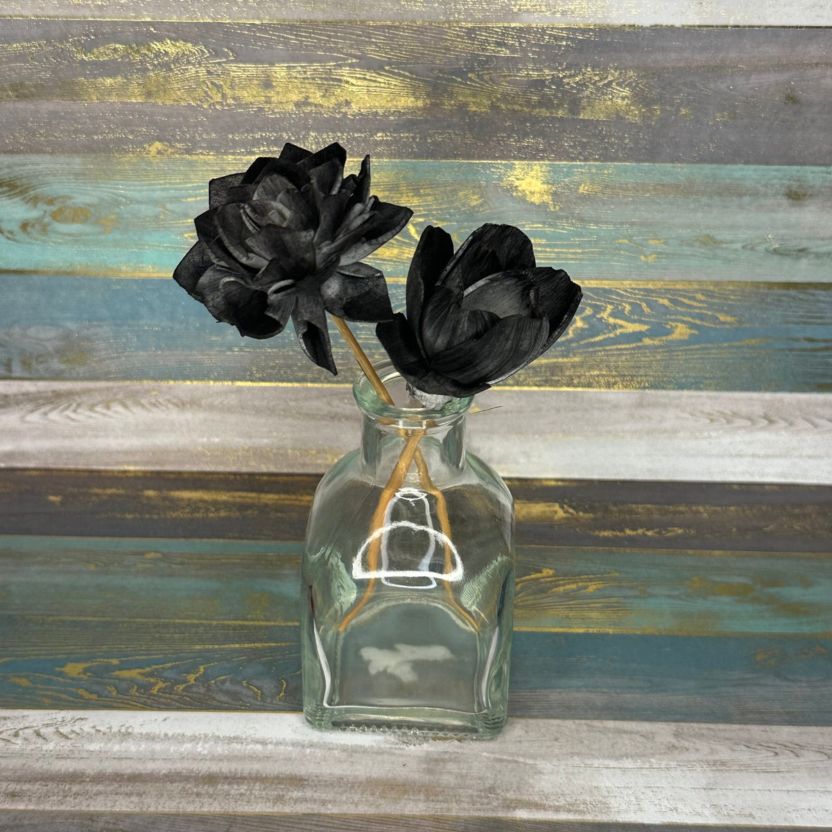 A glass bottle vase holding two black flowers against a textured background.
