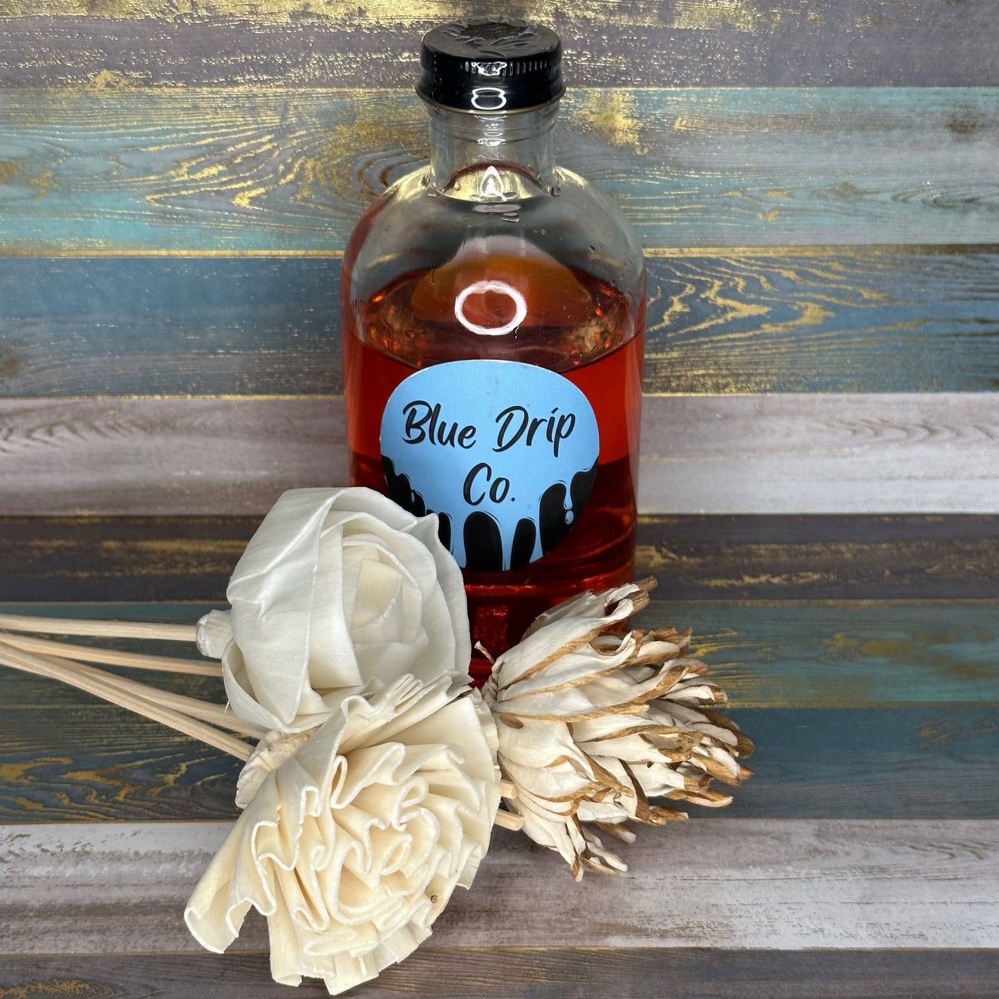 A bottle of Blue Drip Co. liquid alongside decorative flowers.