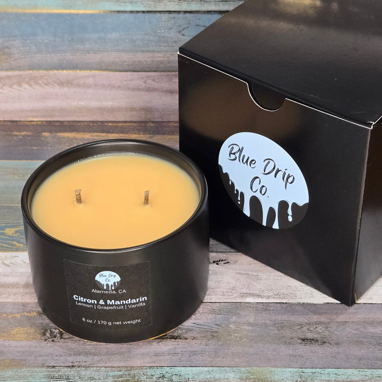 A black candle labeled 'Citron & Mandarín' in a jar with two wicks, next to its matching black box from Blue Drip Co.