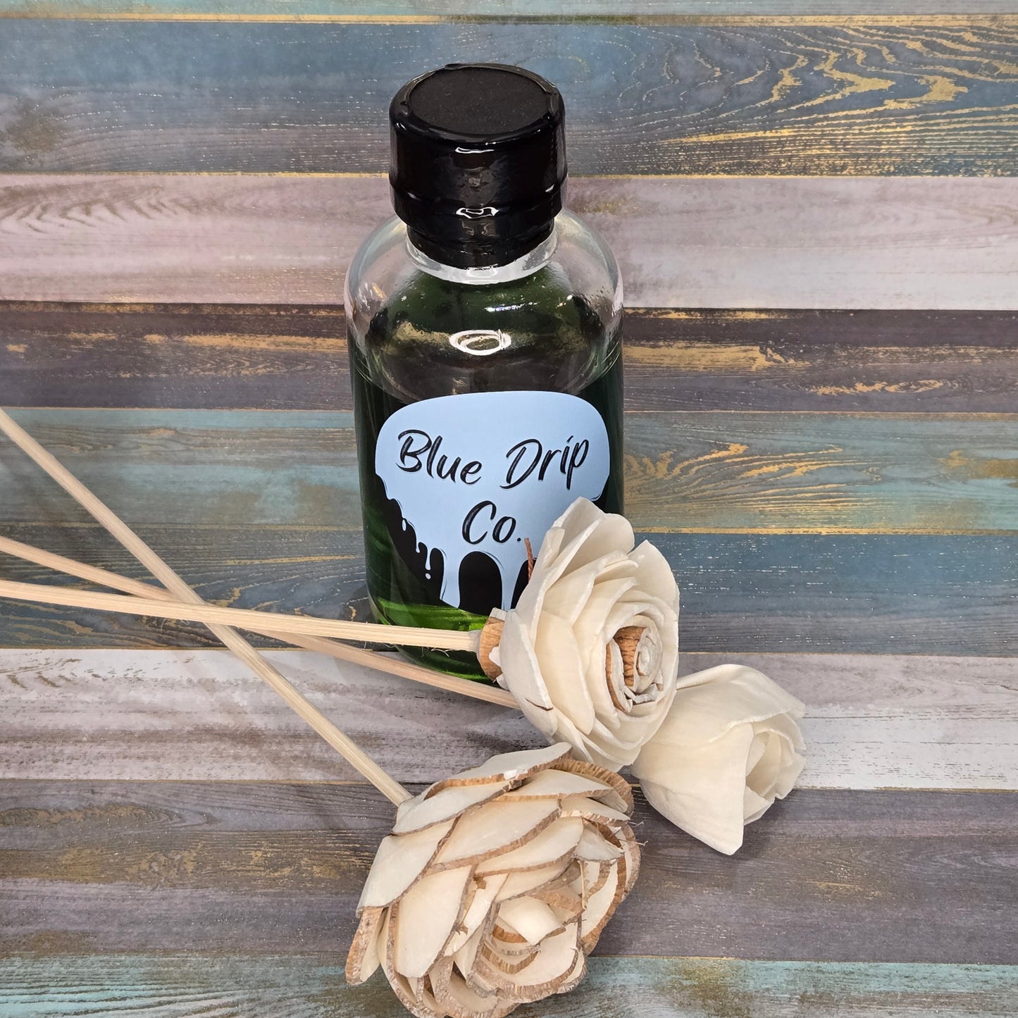 A bottle labeled 'Blue Drip Co.' next to two decorative flowers on a wooden surface.