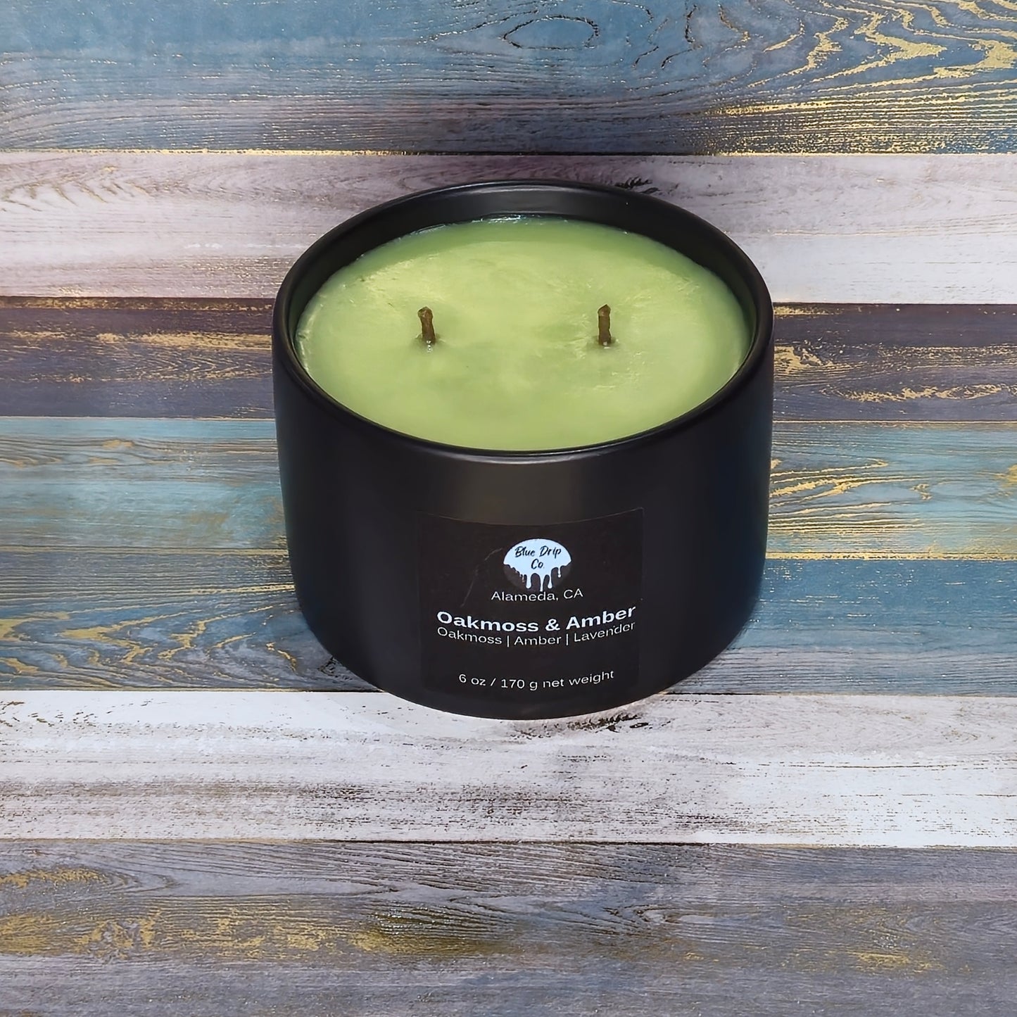 Black two-wick candle with green wax and label on a wooden background