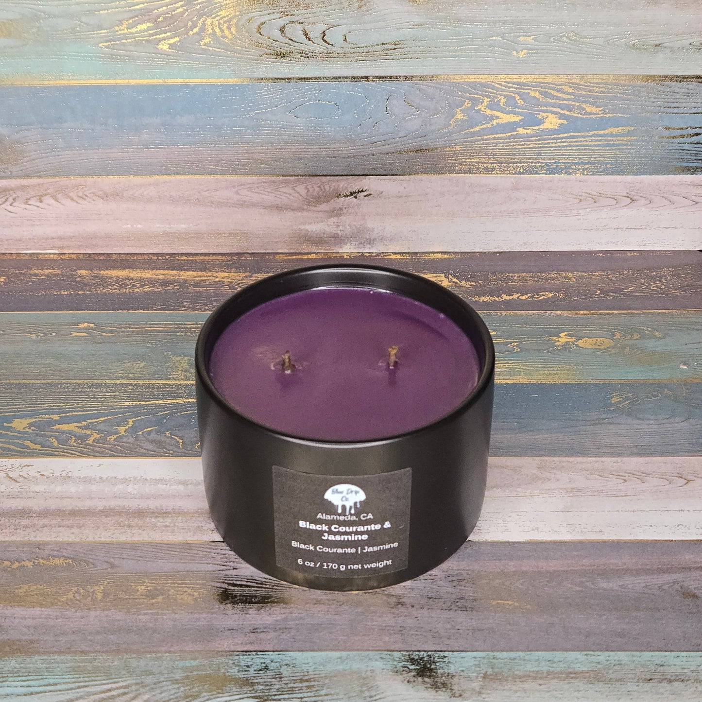 A black candle with two wicks and a lavender color, set against a colorful wooden background.