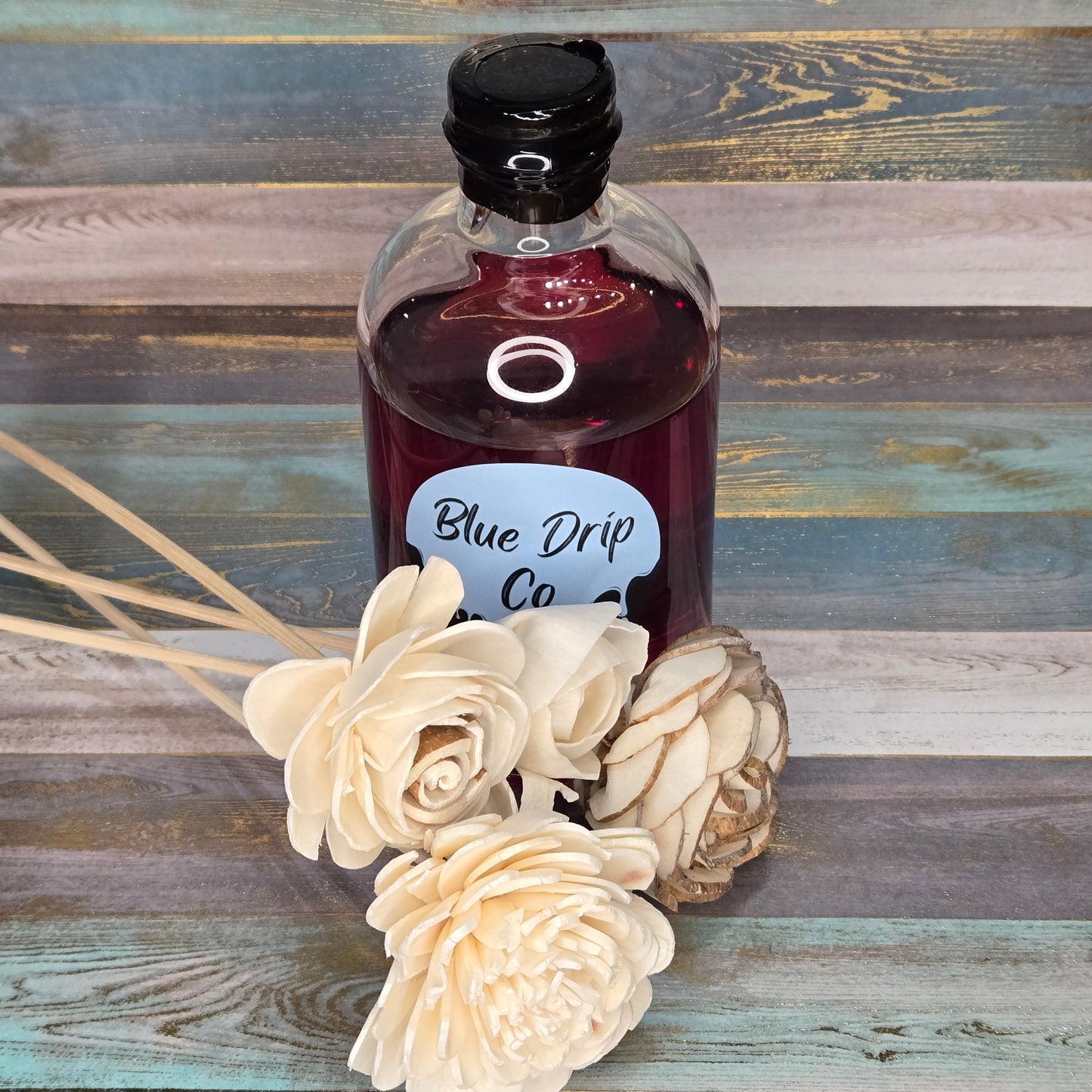 A bottle labeled 'Blue Drip Co' next to white decorative flowers on a wooden surface.
