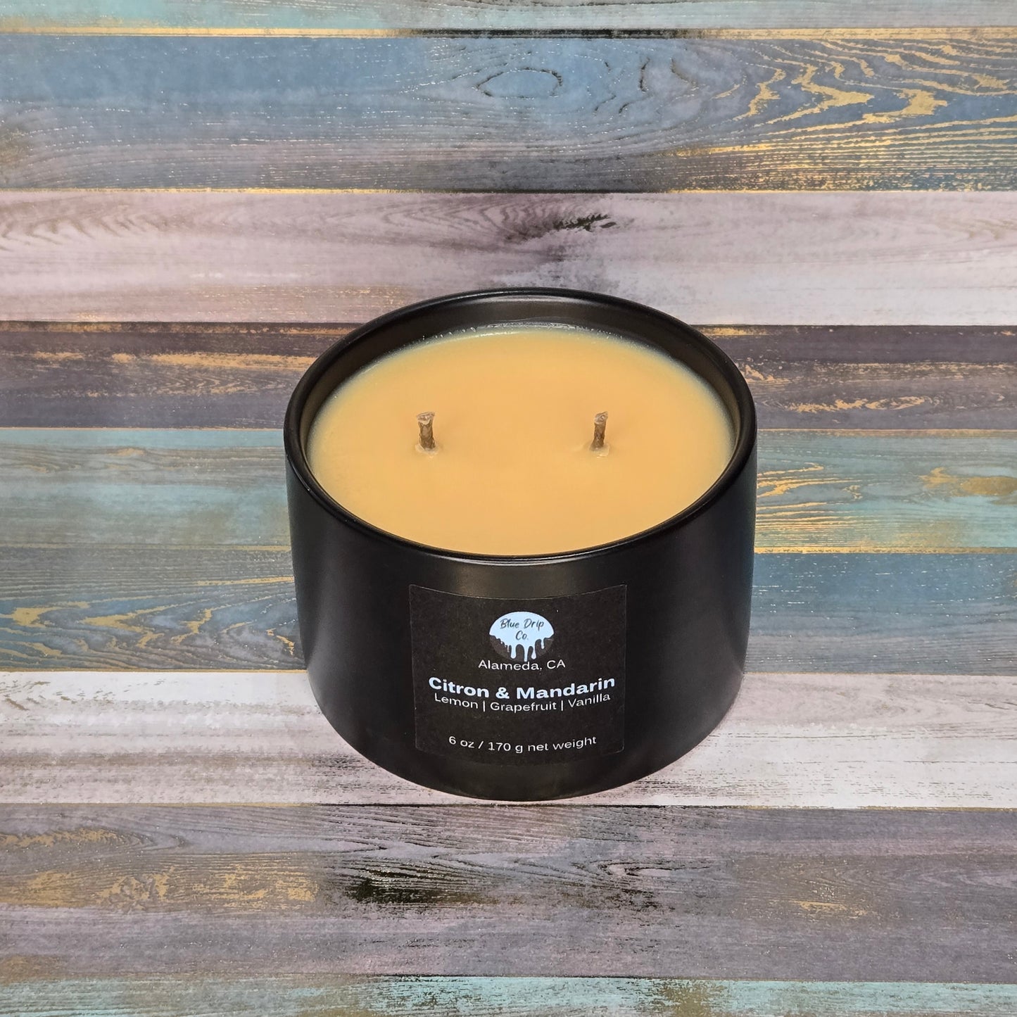 Black candle jar with two wicks and label on a colorful wooden background