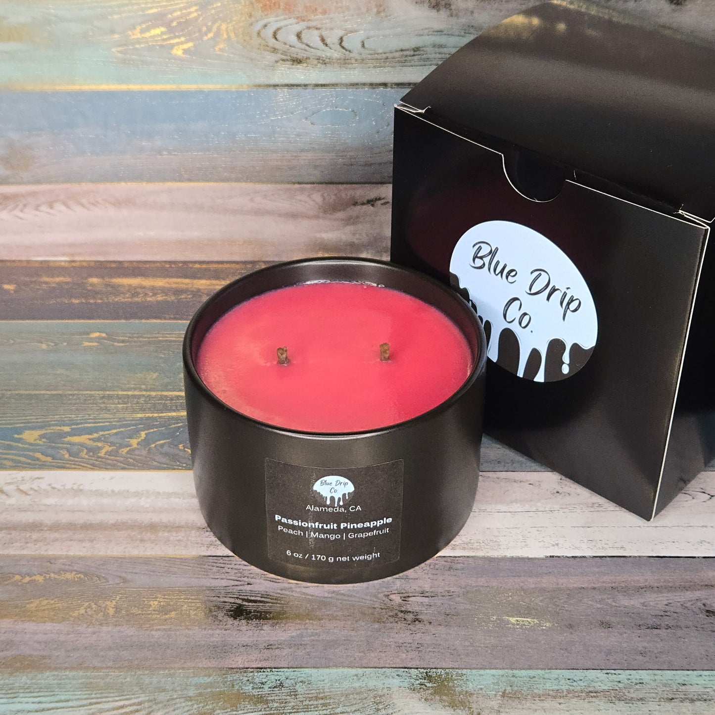 A pink scented candle in a black container next to its packaging from Blue Drip Co.