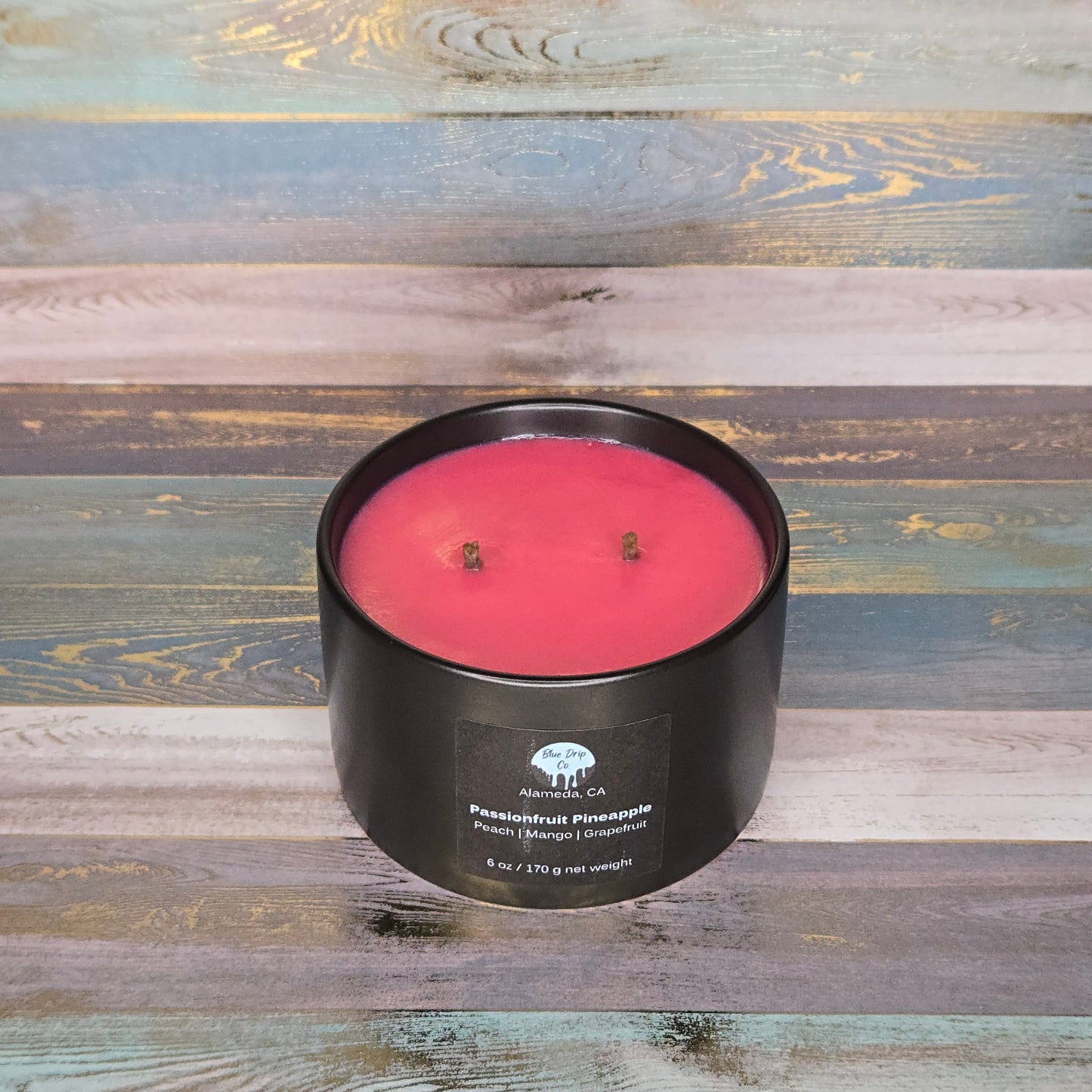 A round, pink candle in a black container placed on a wooden surface.