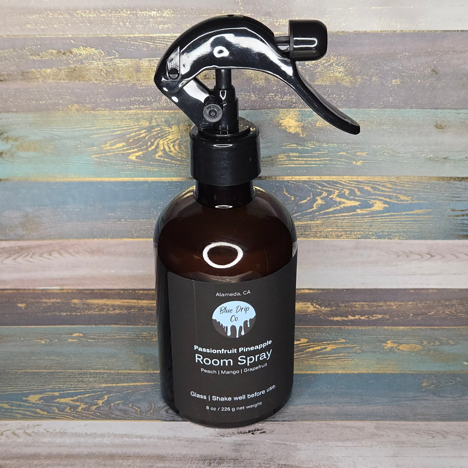 Brown glass bottle of room spray with a black spray nozzle against a colorful wooden background.