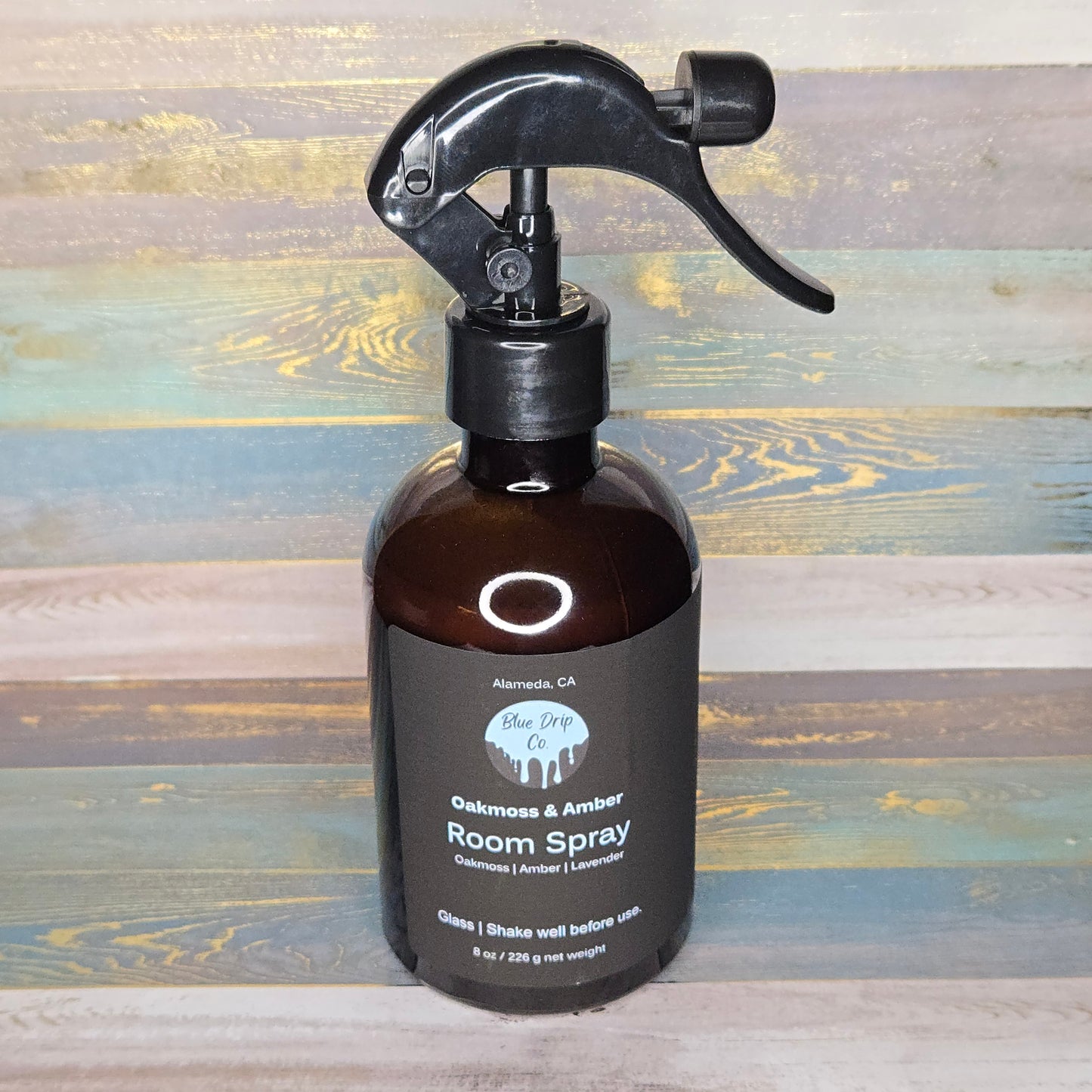 Brown glass bottle of room spray with a black spray nozzle on a rustic wooden background.