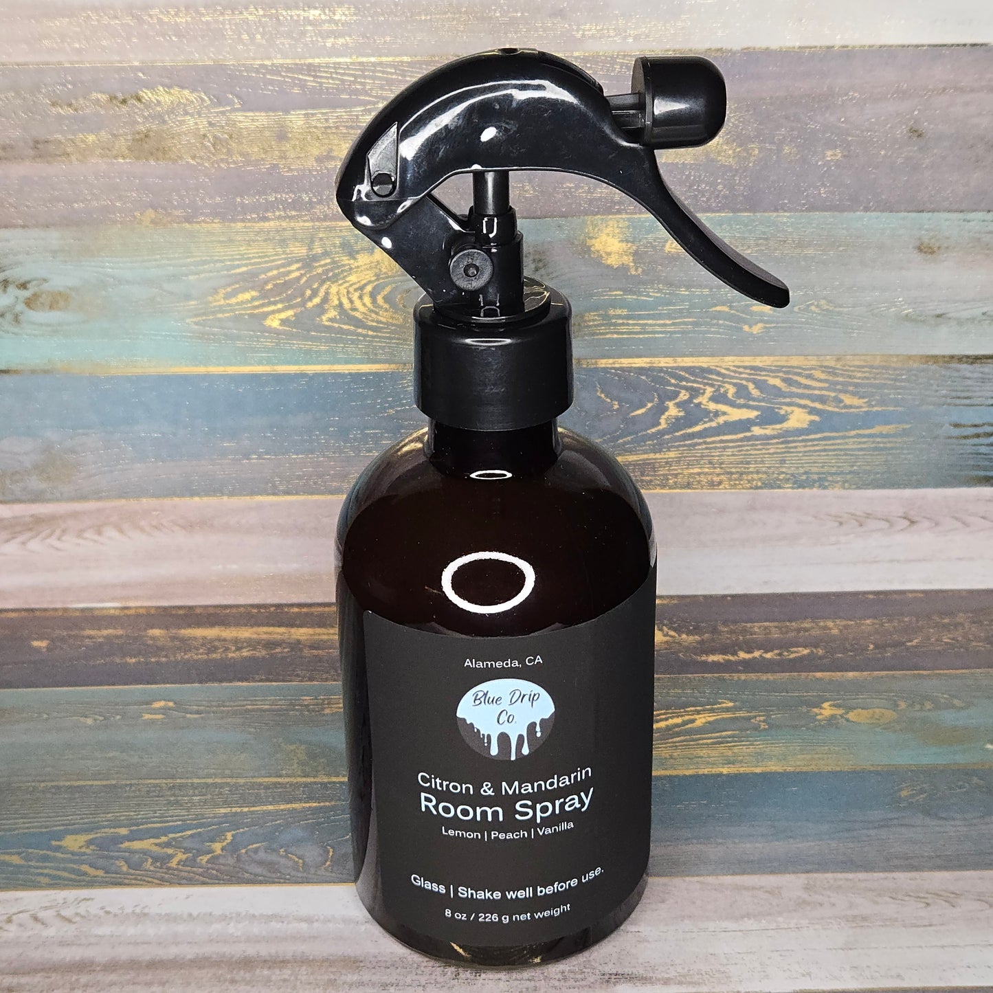 A dark glass bottle of Citron & Mandarin room spray with a black spray nozzle on a wooden background.