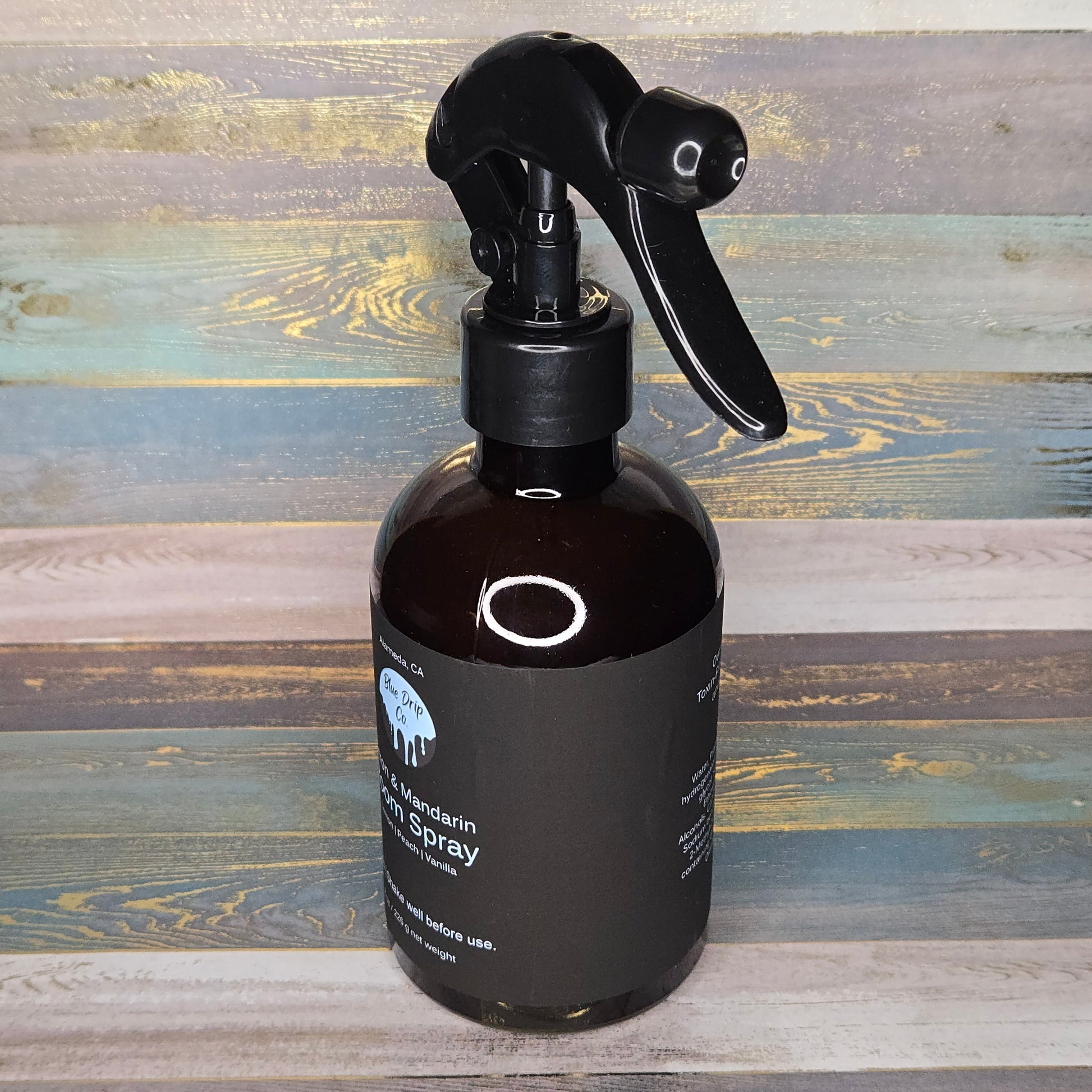 A dark glass spray bottle with a black nozzle on a rustic wooden background.