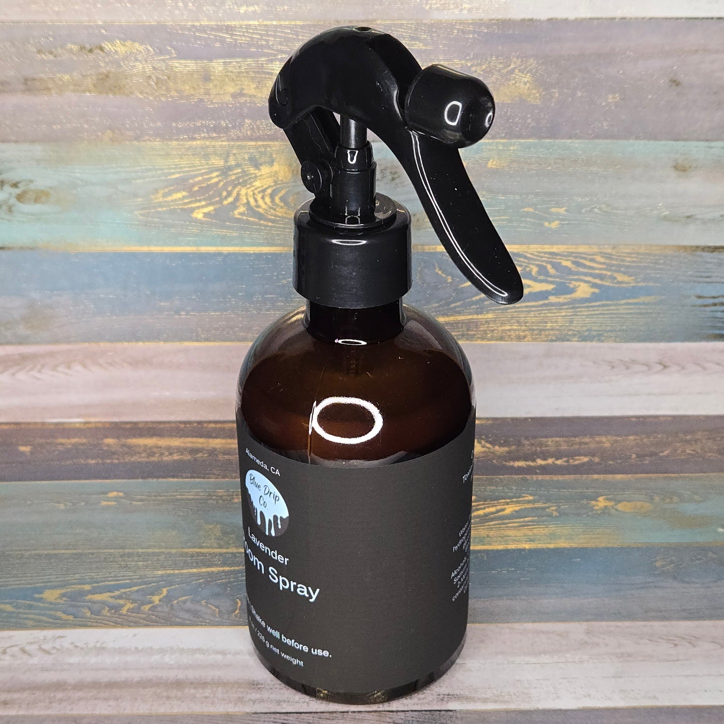 Brown glass spray bottle with a black trigger nozzle on a colorful wooden background.