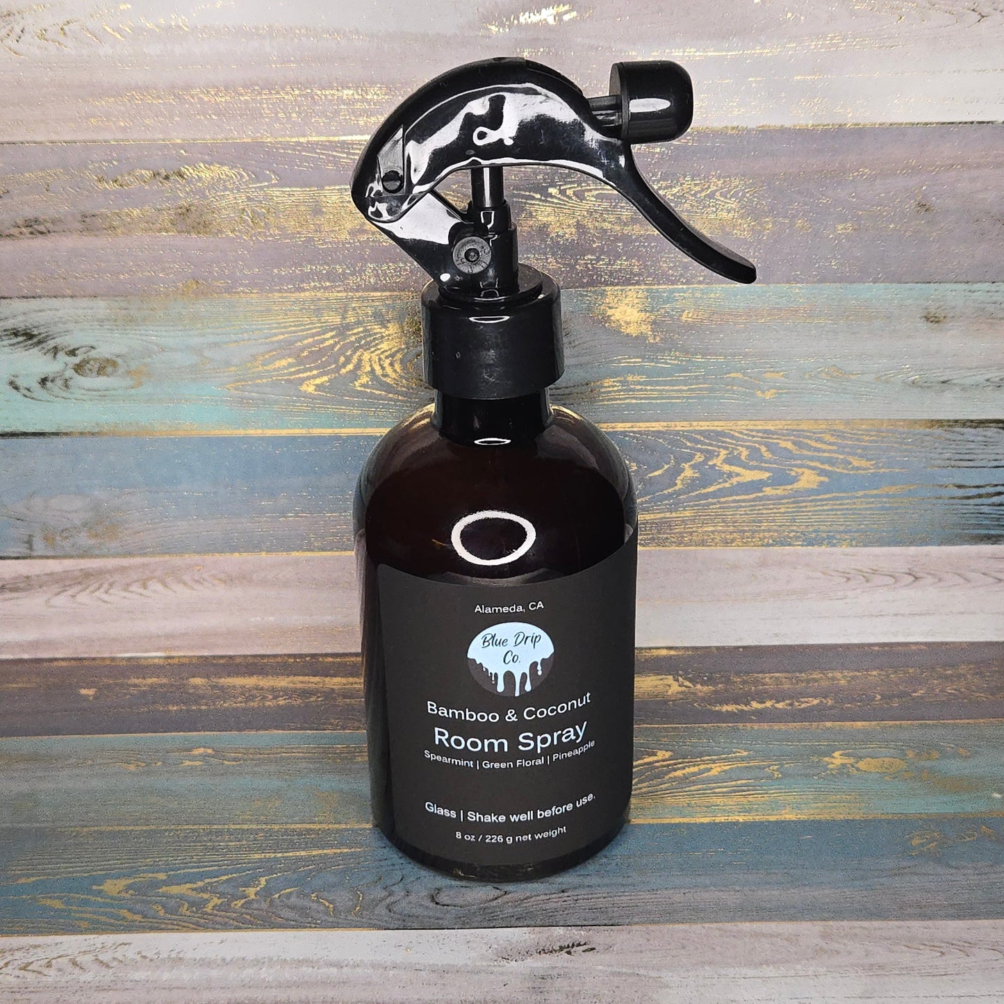 A bottle of Bamboo & Coconut Room Spray with a black spray nozzle on a wooden background.