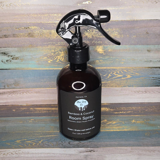 A bottle of Bamboo & Coconut Room Spray with a black spray nozzle on a wooden background.